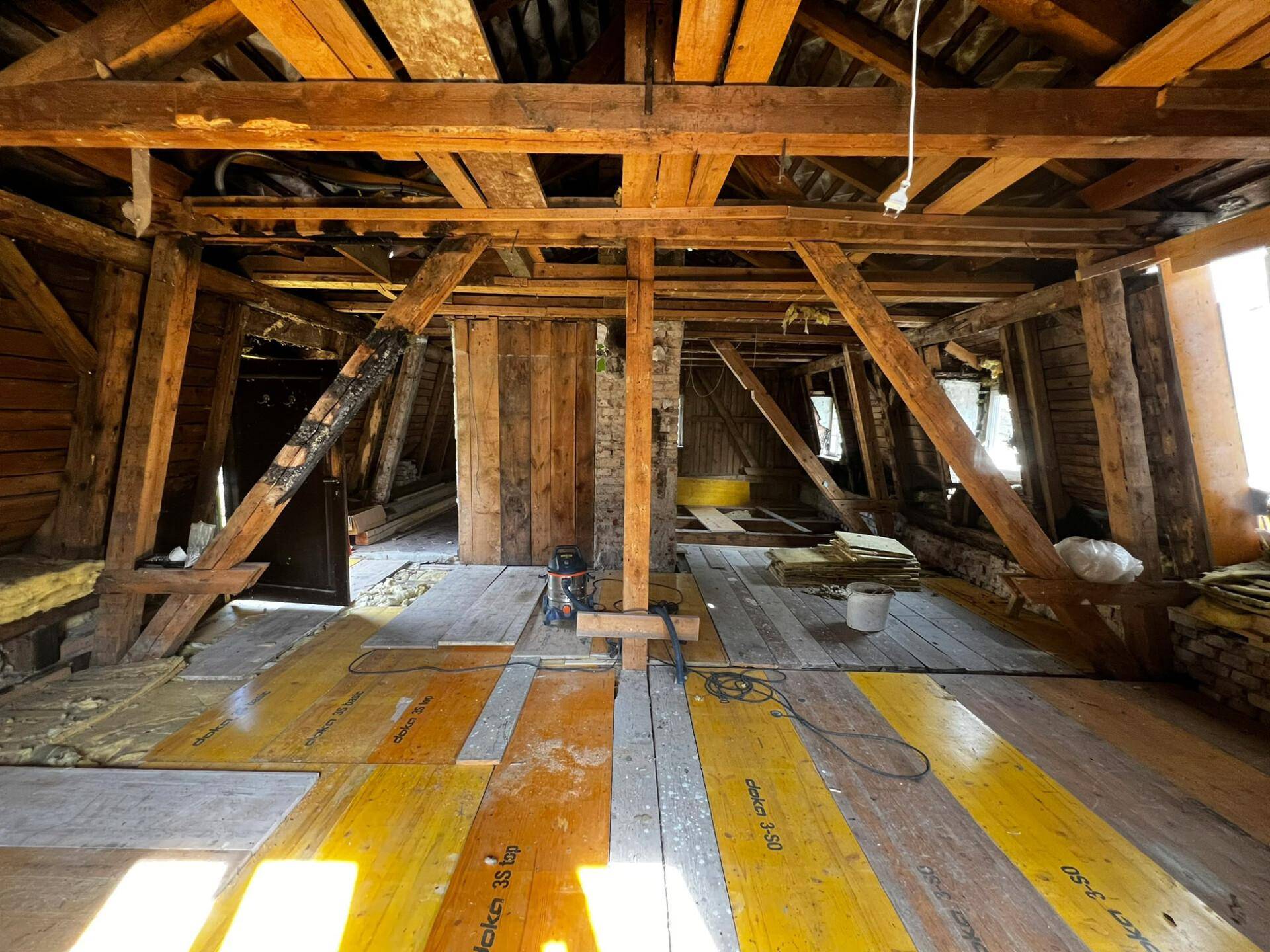 Dachboden im Umbau mit freiliegenden Holzbalken und neuer Bodenisolierung.