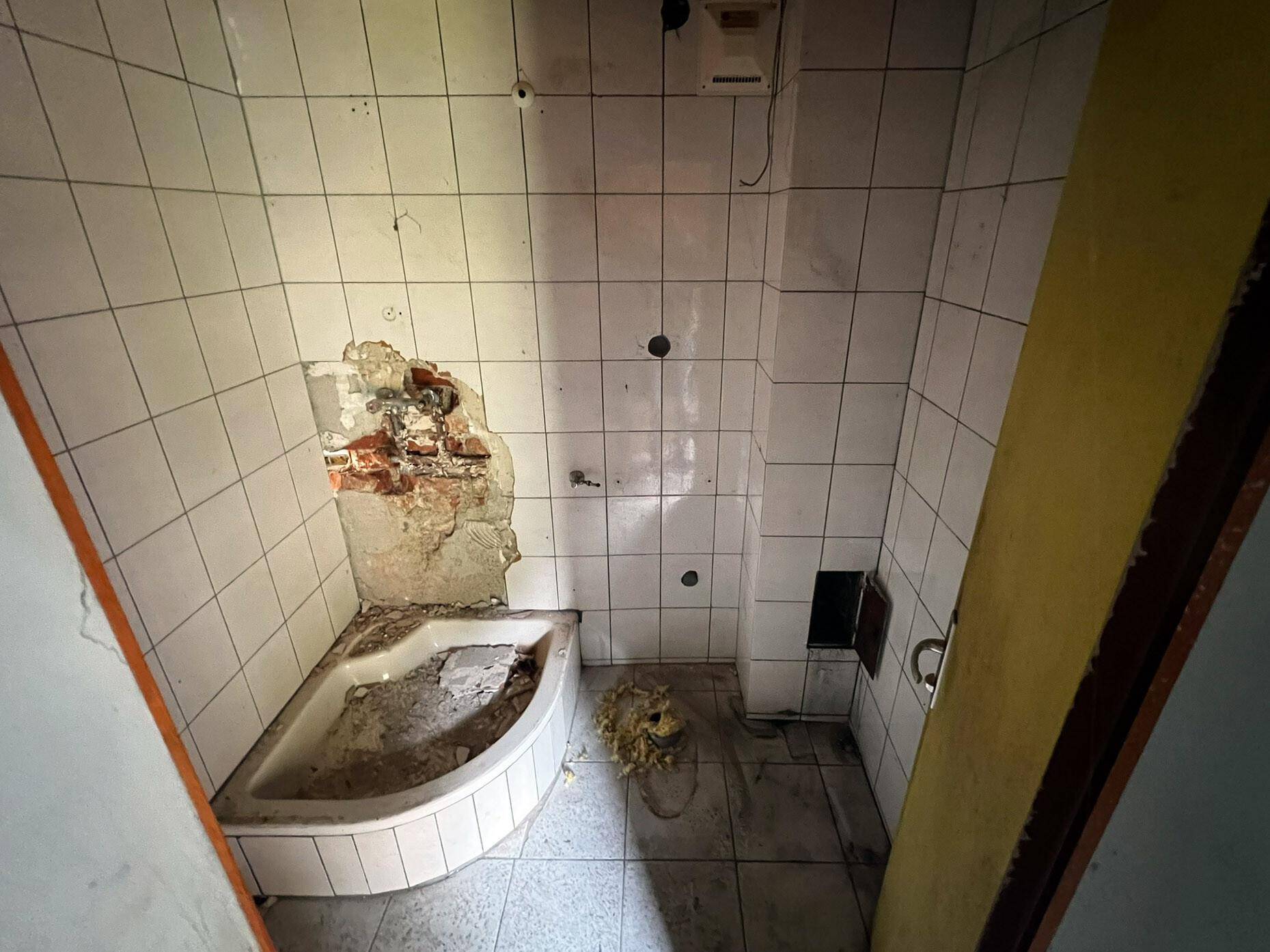 Badezimmer im Umbau mit weißen Fliesen, einer Eckbadewanne und freigelegtem Mauerwerk.