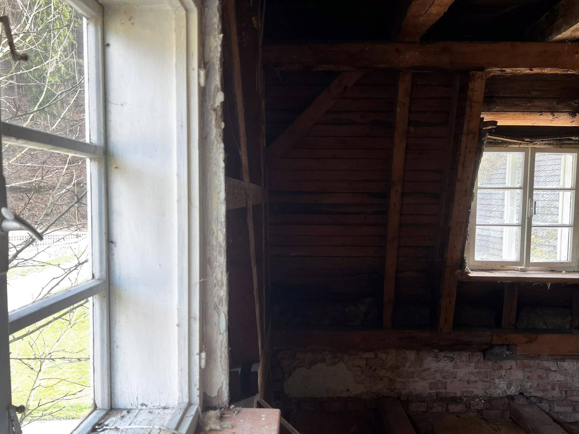 Dachboden in Rohzustand mit sichtbaren Holzbalken und zwei Fenstern, bereit für den Ausbau.
