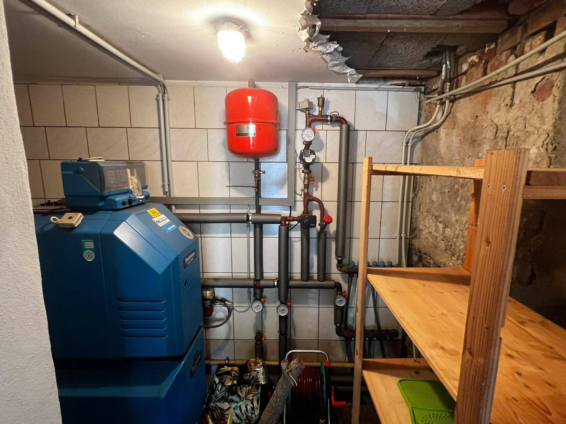 Heizungsraum mit blauem Heizkessel, rotem Ausdehnungsgefäß und sichtbaren Rohrleitungen.