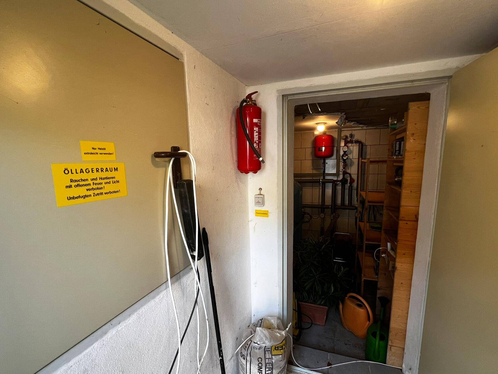 Eingangsbereich zu einem Öllagerraum mit Feuerlöscher und Warnhinweisen an der Wand.