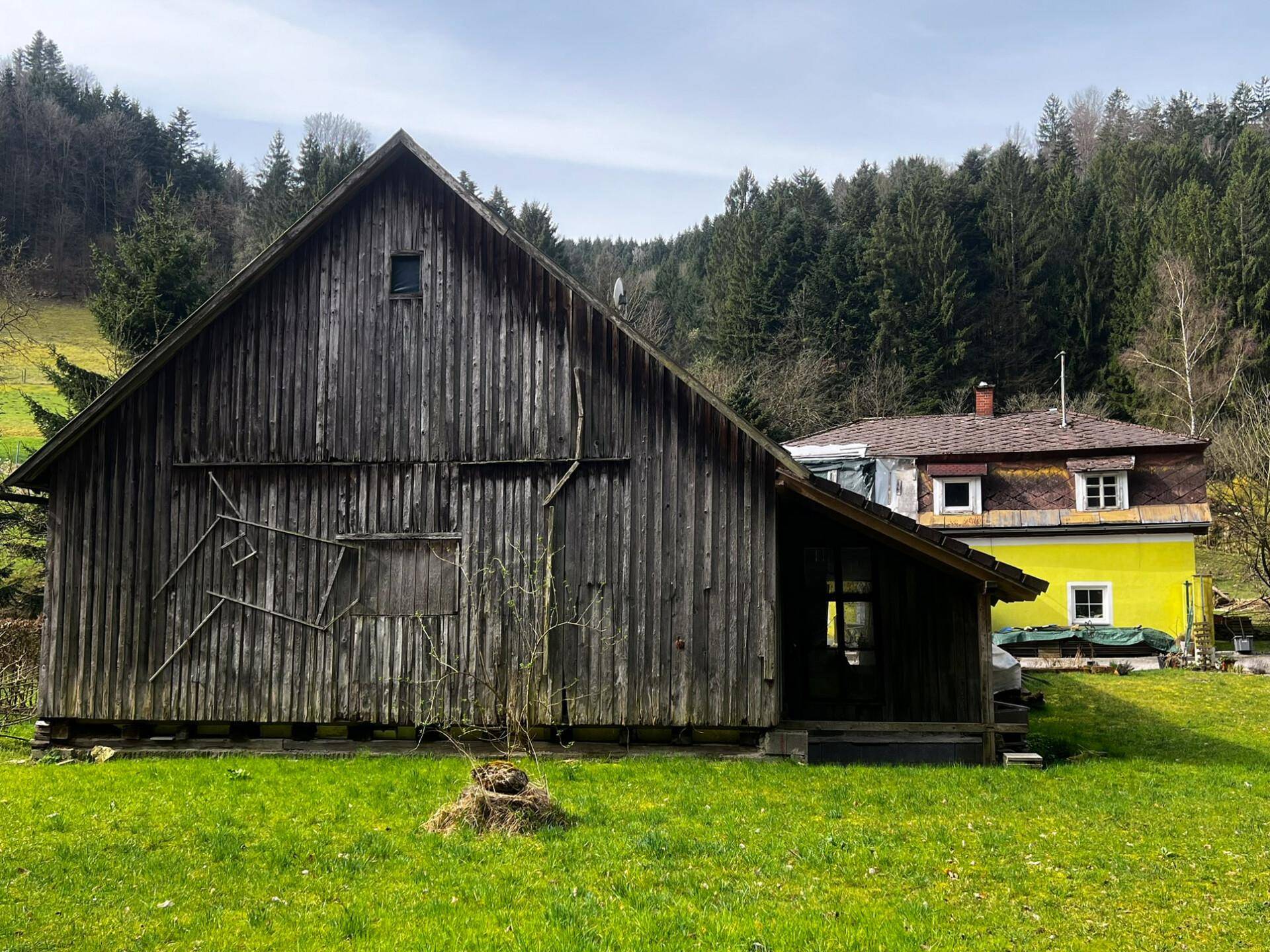 Großes Holzgebäude mit grüner Wiese im Vordergrund und einem weiteren Haus im Hintergrund.