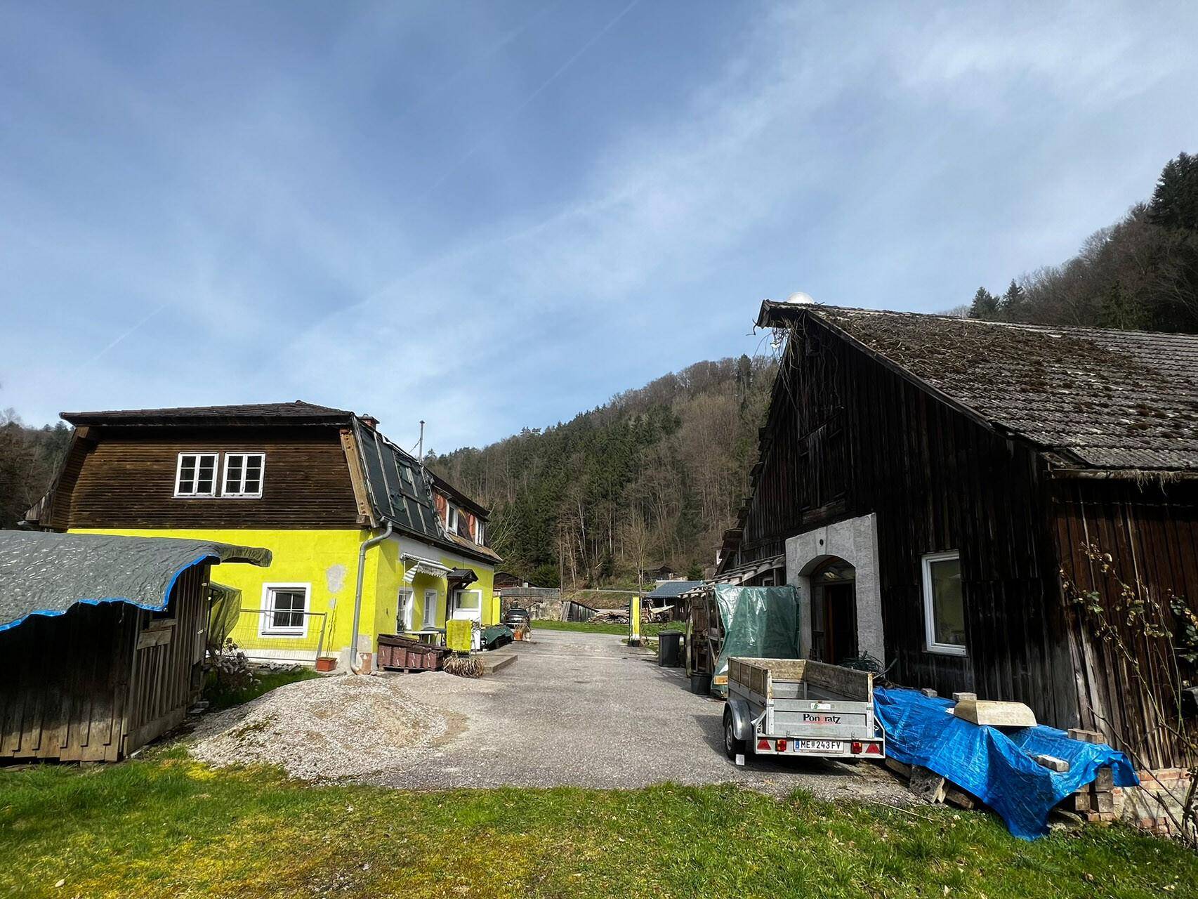 Ländliches Anwesen mit zwei älteren Gebäuden, umgeben von grünen Hügeln und Bäumen.