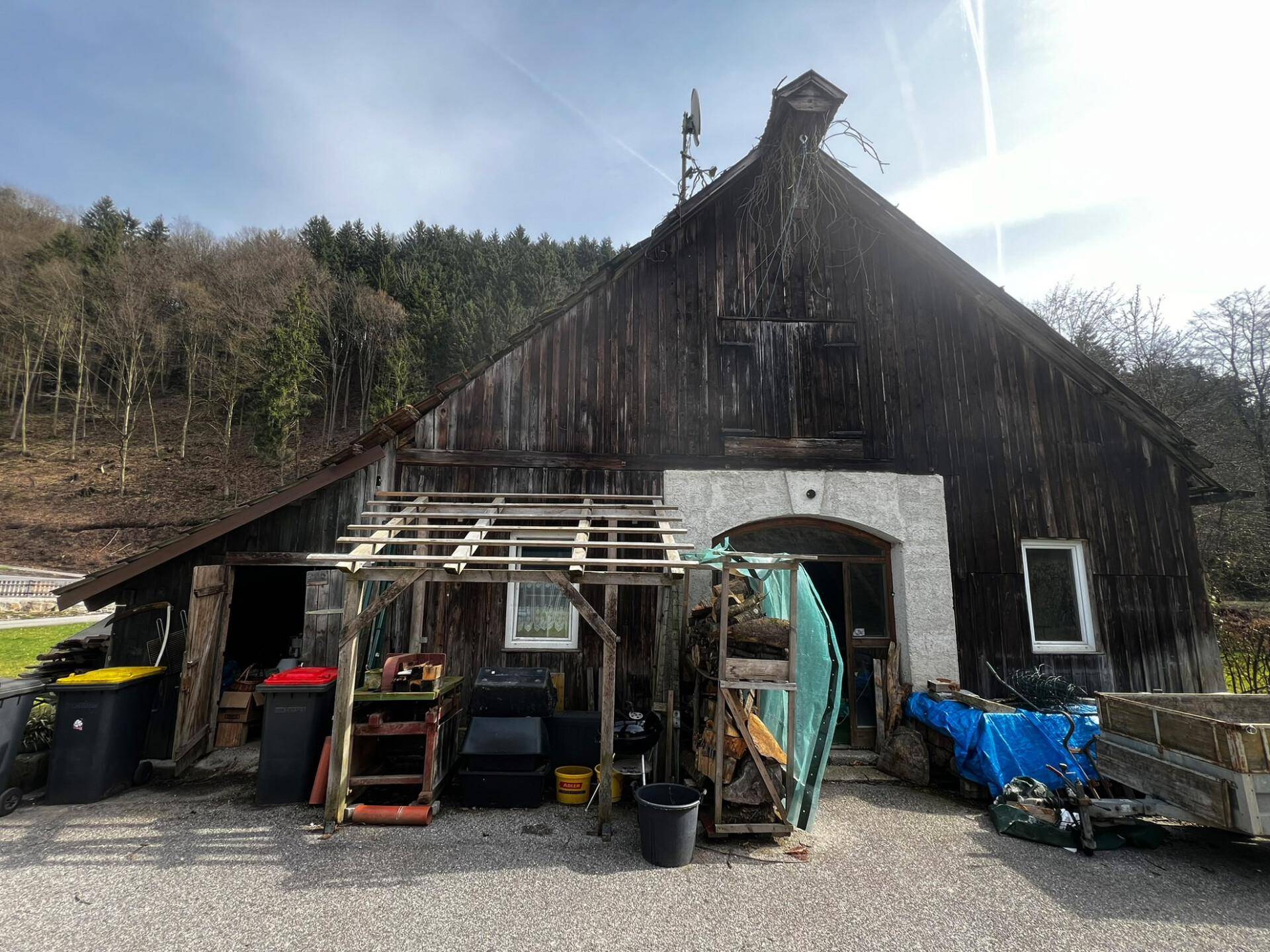 Altes Holzgebäude mit einem überdachten Eingangsbereich und verschiedenen Gegenständen davor.