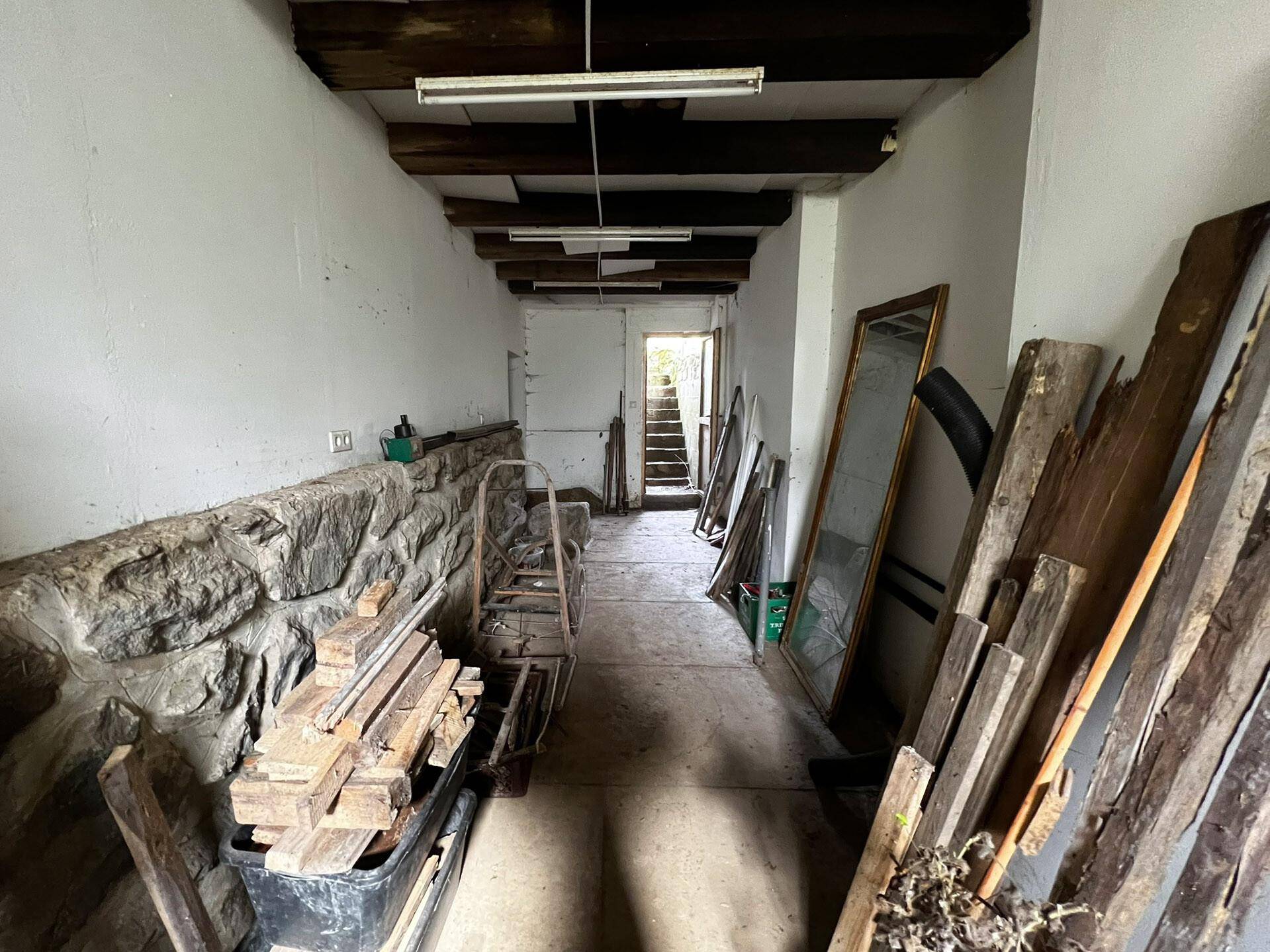 Langer Kellerraum mit sichtbaren Holzbalken an der Decke und einer Steinwand auf einer Seite.