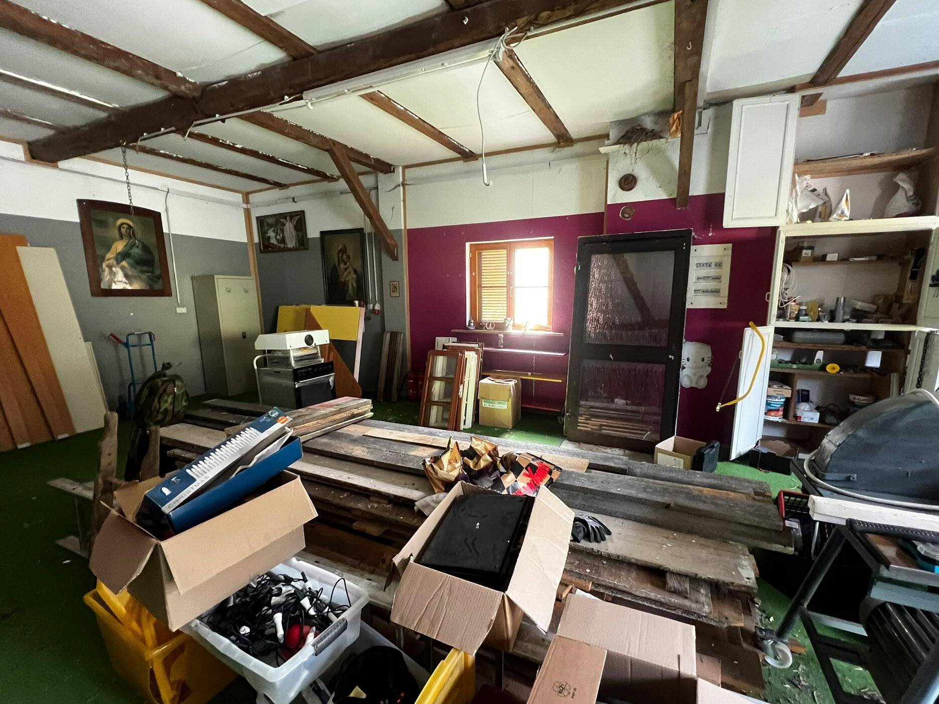 Werkstatt oder Lagerraum mit vielen Gegenständen, Holzbalken und einem kleinen Fenster.