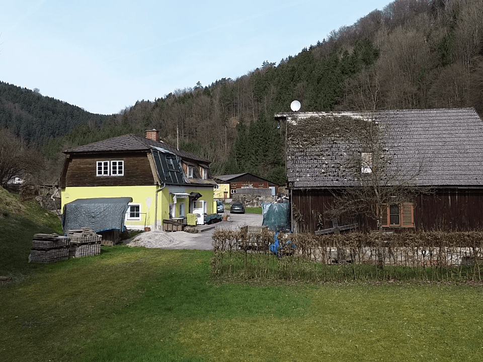Weitläufiges Anwesen mit zwei Gebäuden, umgeben von grünen Wiesen und bewaldeten Hügeln.