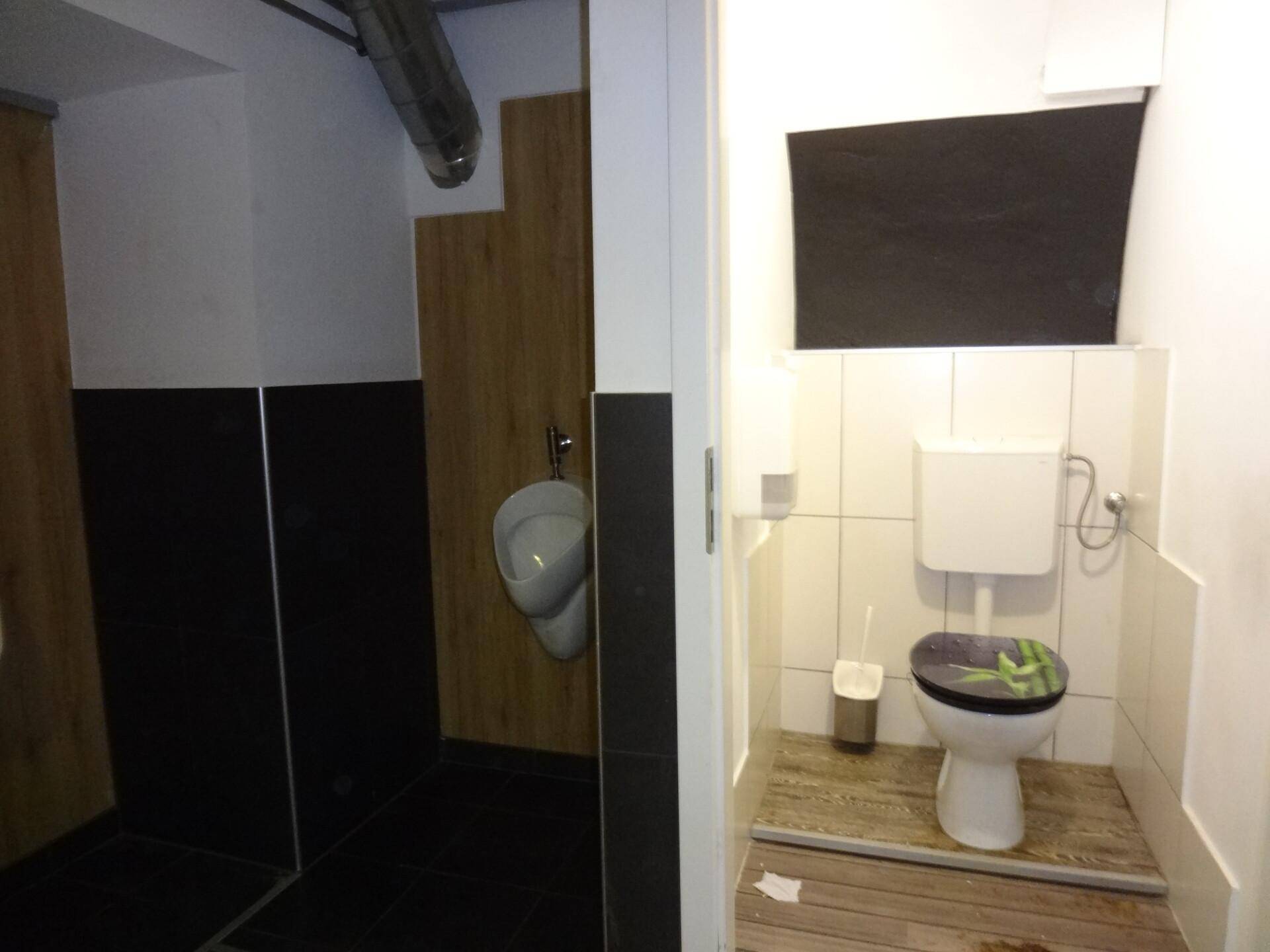 Zwei separate Toilettenkabinen mit Urinal und WC, ausgestattet mit Fliesen und Holzverkleidung.