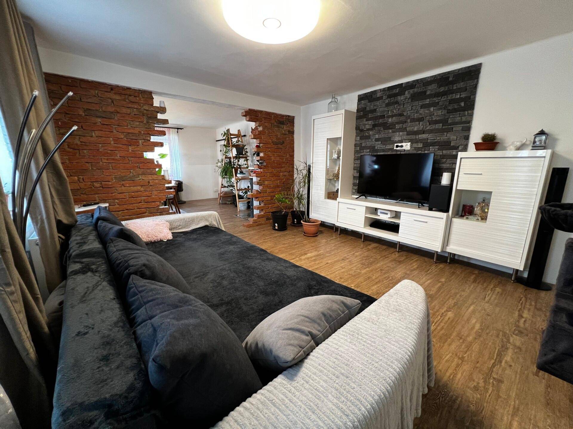 Gemütliches Wohnzimmer mit dunklem Sofa, modernem TV-Möbel und dekorativen Ziegelwänden.