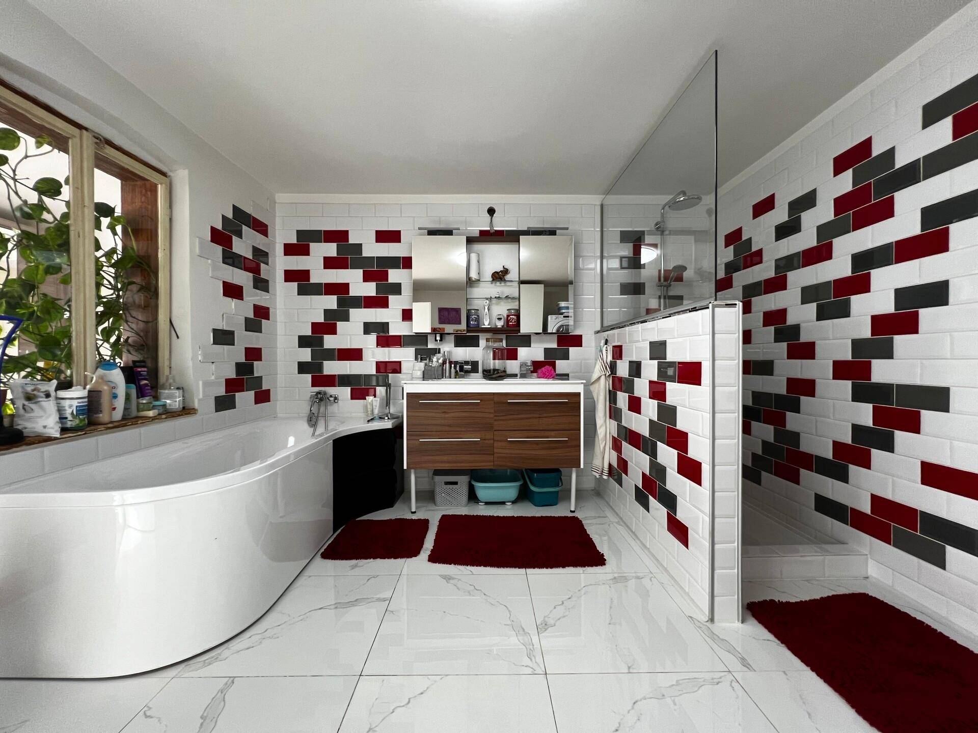Modernes Badezimmer mit Badewanne, begehbarer Dusche und auffälligen rot-schwarz-weißen Fliesen.
