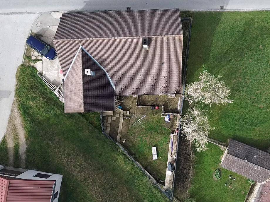 Luftaufnahme des Anwesens mit Haus, Garten und angrenzenden Grünflächen sowie einer Straße.