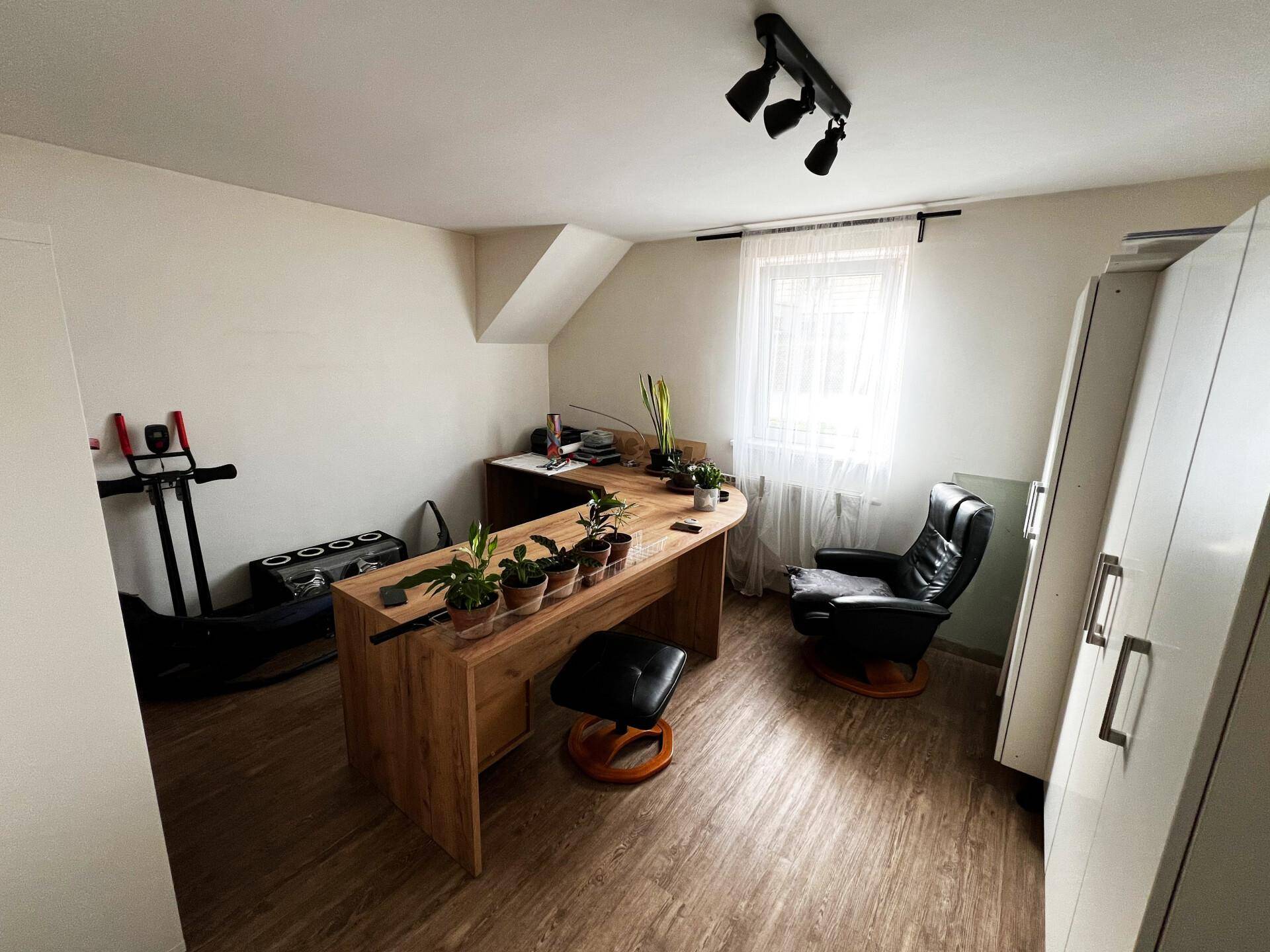 Arbeitszimmer mit Holzschreibtisch, Bürostuhl und Fitnessgeräten unter einer Dachschräge.