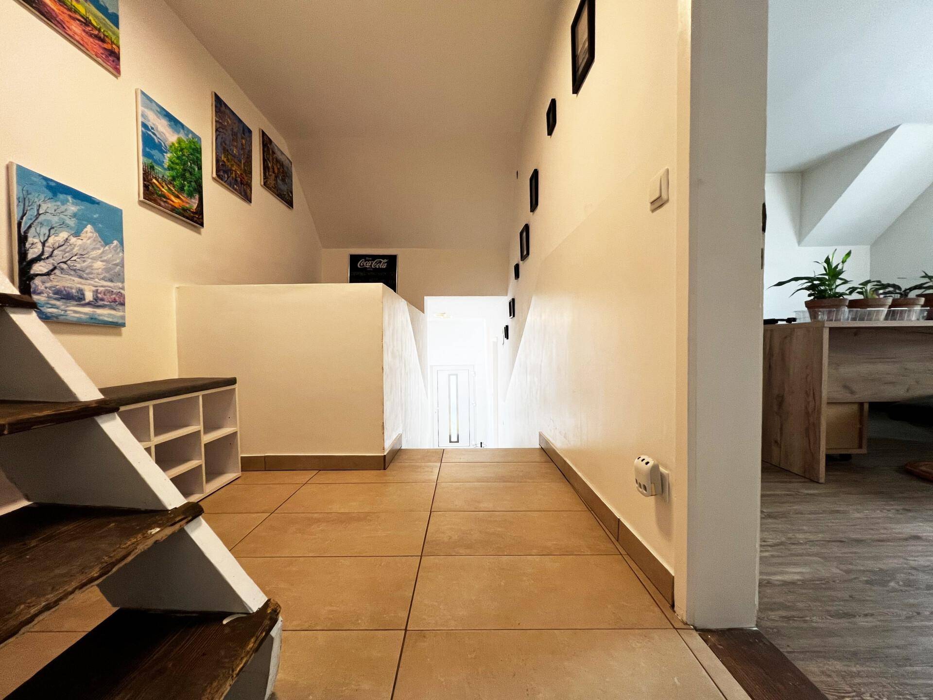 Heller Flur mit gefliestem Boden, Holztreppe und dekorativen Bildern an der Wand.