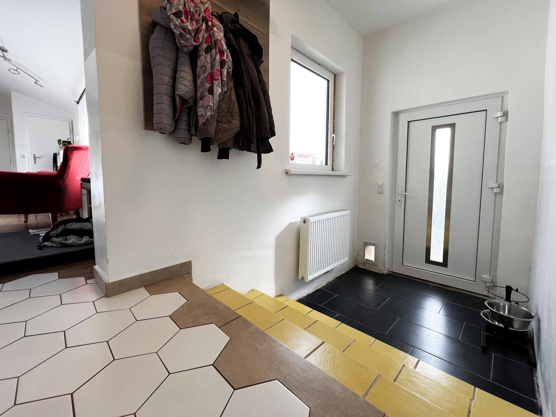 Eingangsbereich mit Garderobe, Heizkörper und Haustür, gekennzeichnet durch unterschiedliche Bodenbeläge.