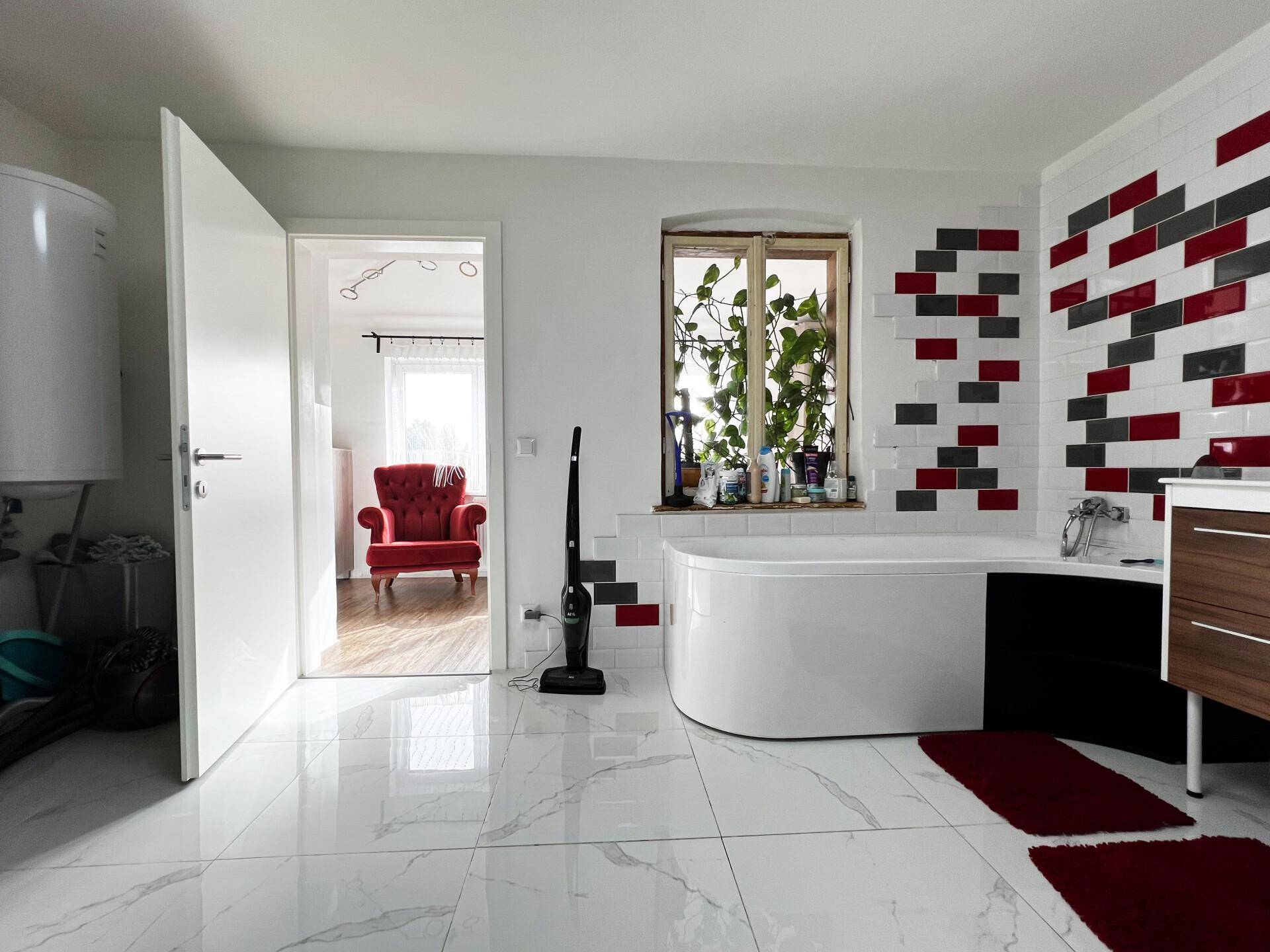 Badezimmer mit Badewanne und Blick in einen angrenzenden Raum mit rotem Sessel.