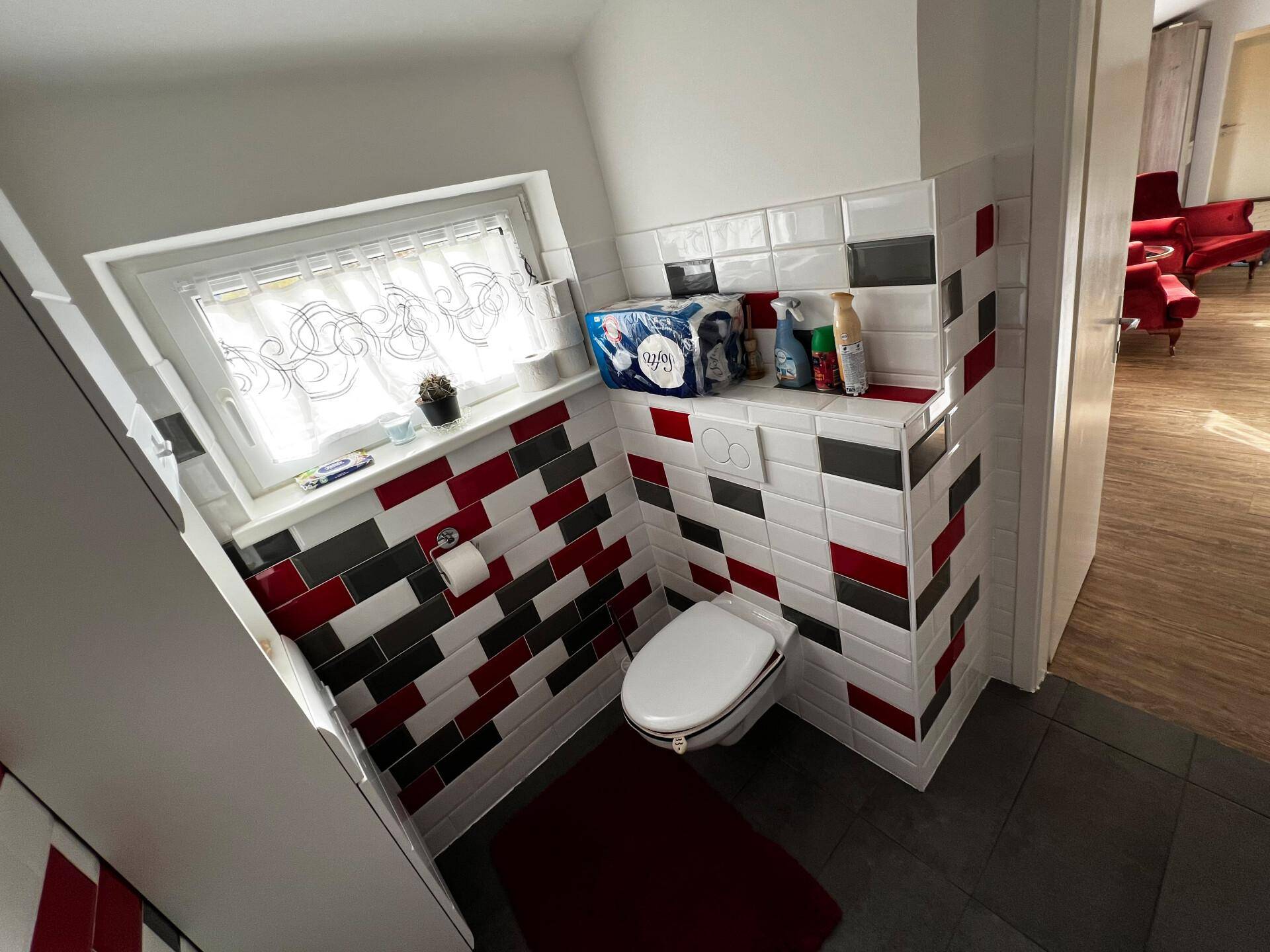 Gäste-WC mit Toilette, Fenster und auffälligen rot-schwarz-weißen Wandfliesen.