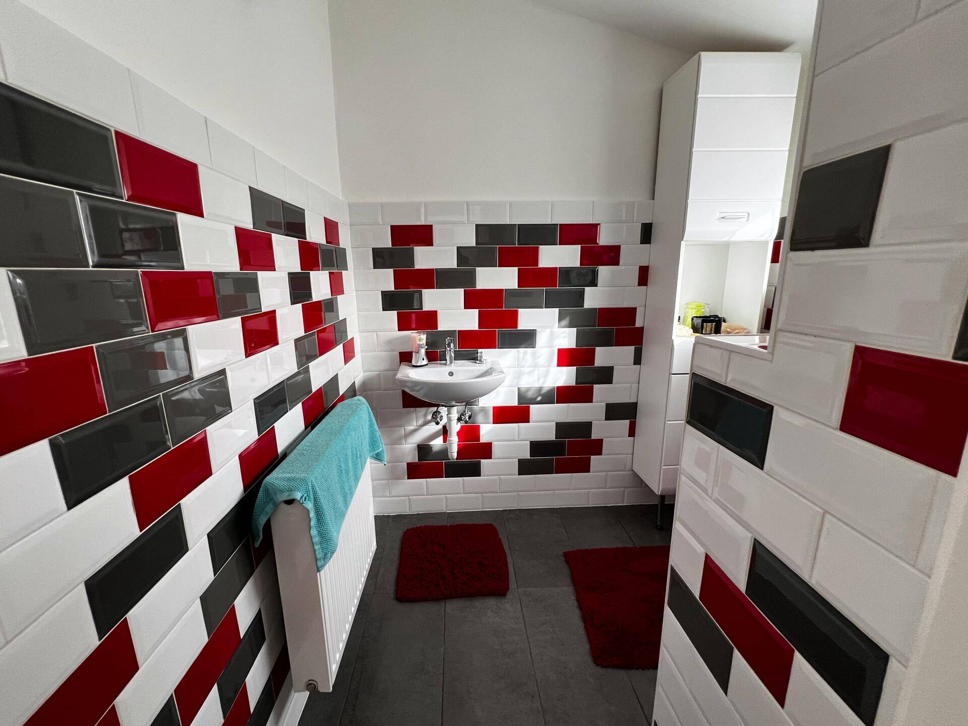 Kleines Gäste-WC mit Waschbecken und farbenfrohen Fliesen in Rot, Schwarz und Weiß.