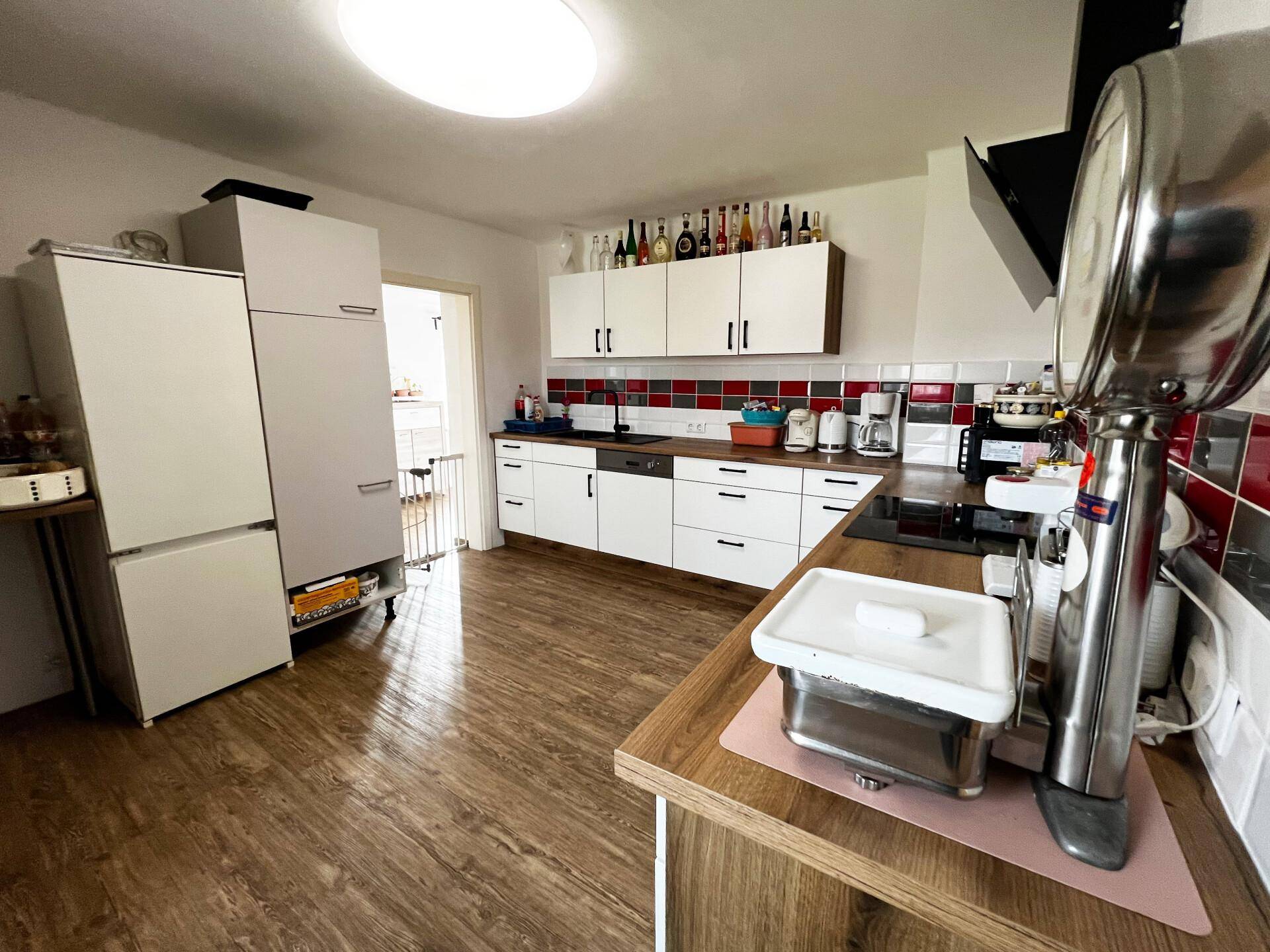 Geräumige Küche mit Kühlschrank, viel Arbeitsfläche und weißen Oberschränken.