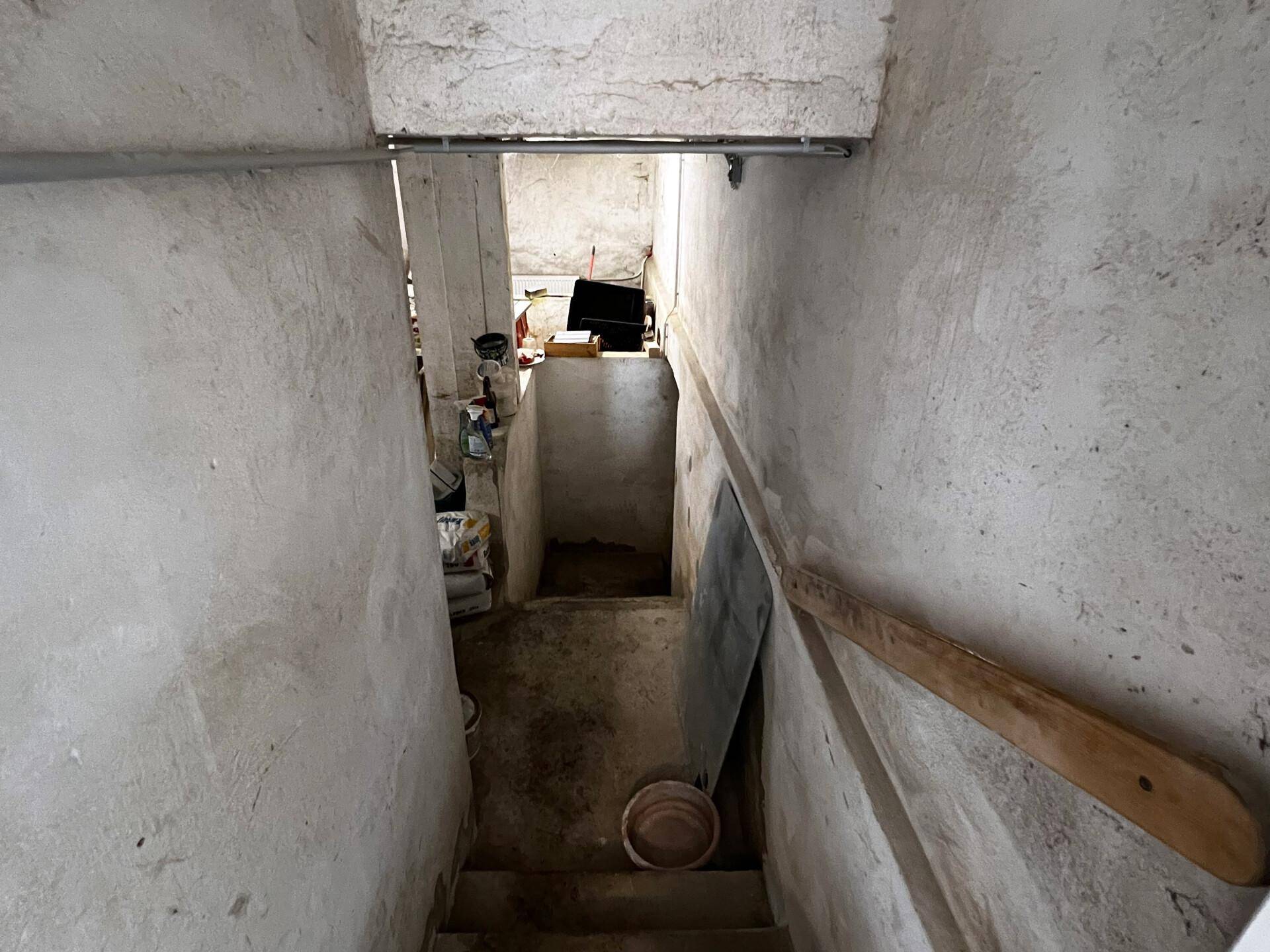 Unfertige Betontreppe führt hinunter in einen Kellerraum mit rauen Wänden.
