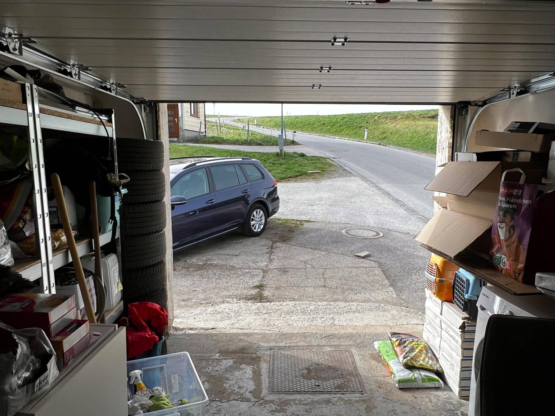 Blick aus der Garage auf die Einfahrt und eine ländliche Straße mit einem geparkten Auto.