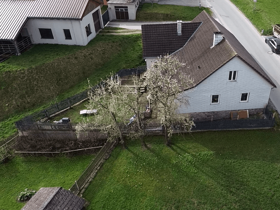 Luftaufnahme eines Hauses mit Garten, umgeben von grünen Flächen und weiteren Gebäuden.