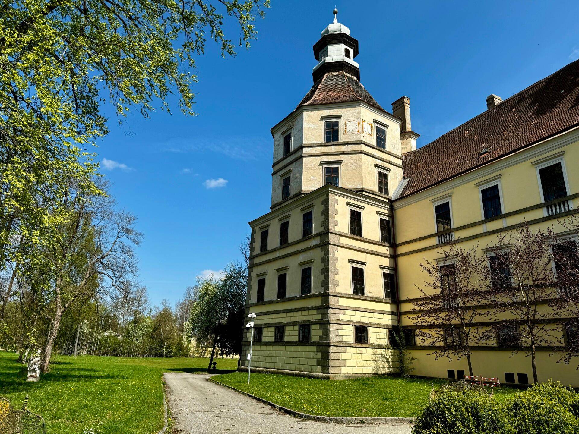 Detailansicht eines Schlossturms mit mehreren Etagen und einem weitläufigen grünen Gelände im Vordergrund.