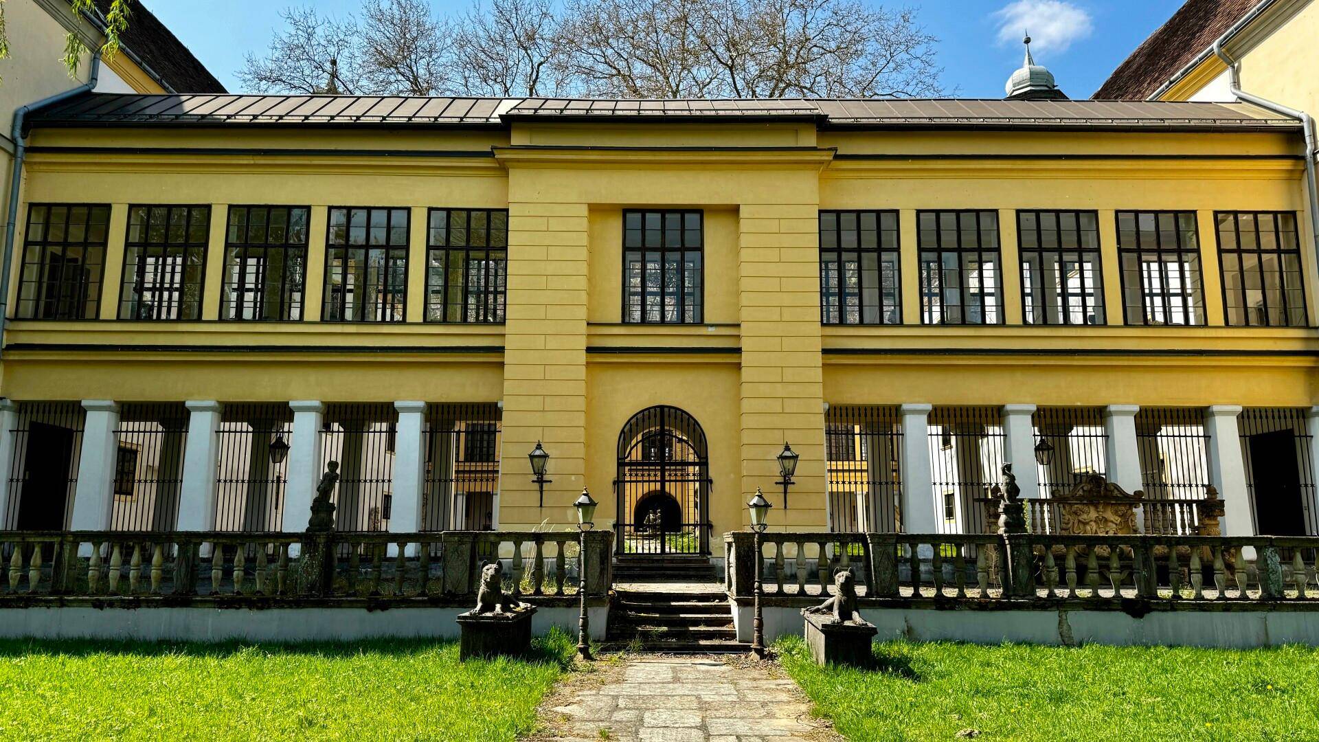 Symmetrische Fassade eines Schlossteils mit vielen Fenstern, Säulen und einem zentralen Eingangsbereich.