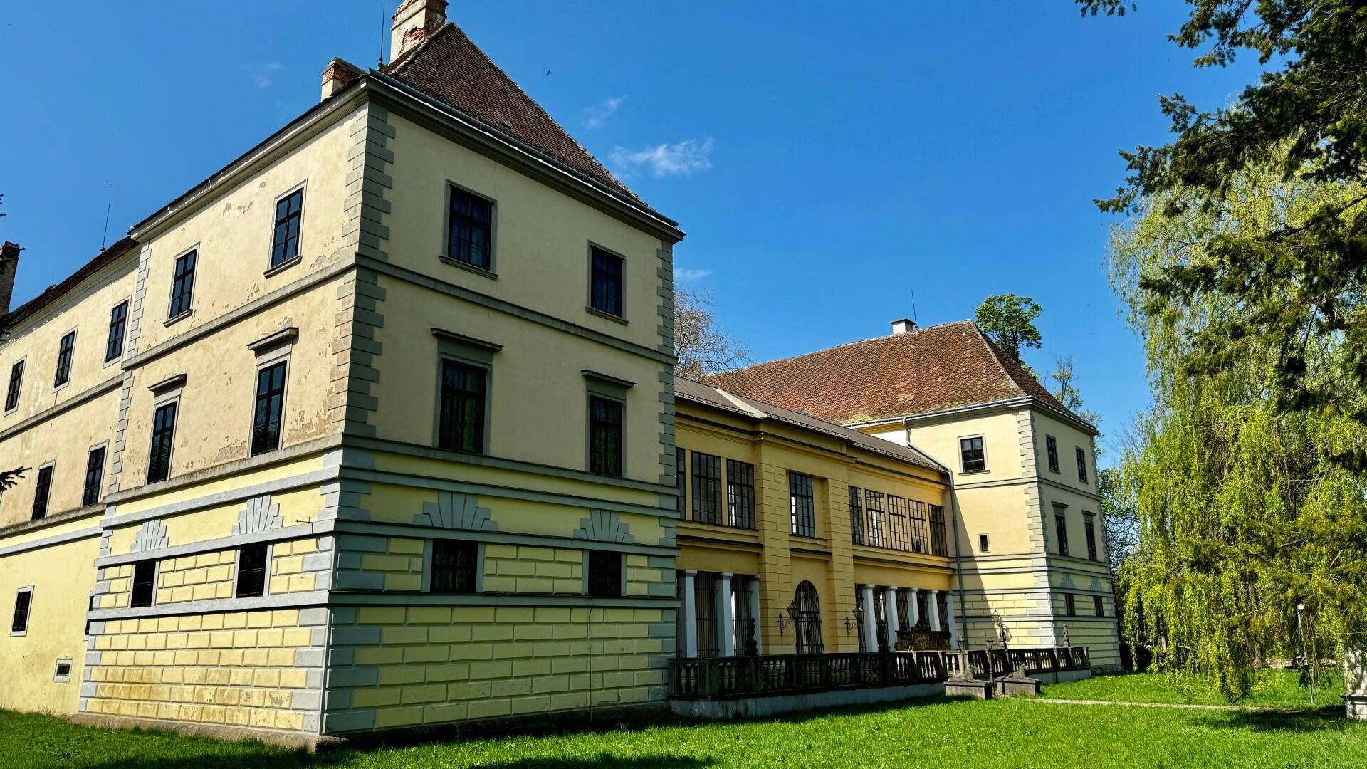 Seitenansicht des historischen Schlosses mit mehreren Flügeln und einem weitläufigen grünen Rasen im Vordergrund.
