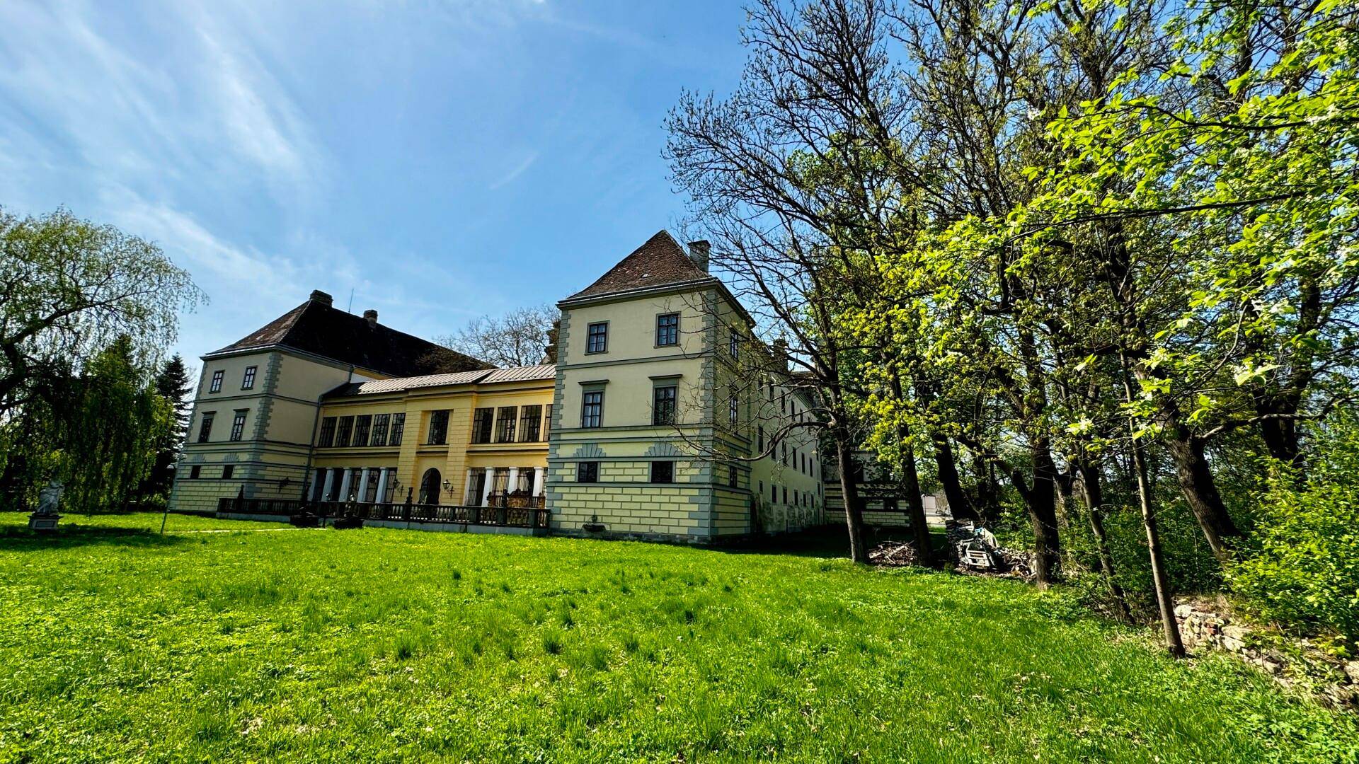 Das Schlossgebäude ist von einem großen, gepflegten Rasen und alten Bäumen umgeben, die eine ruhige Atmosphäre schaffen.