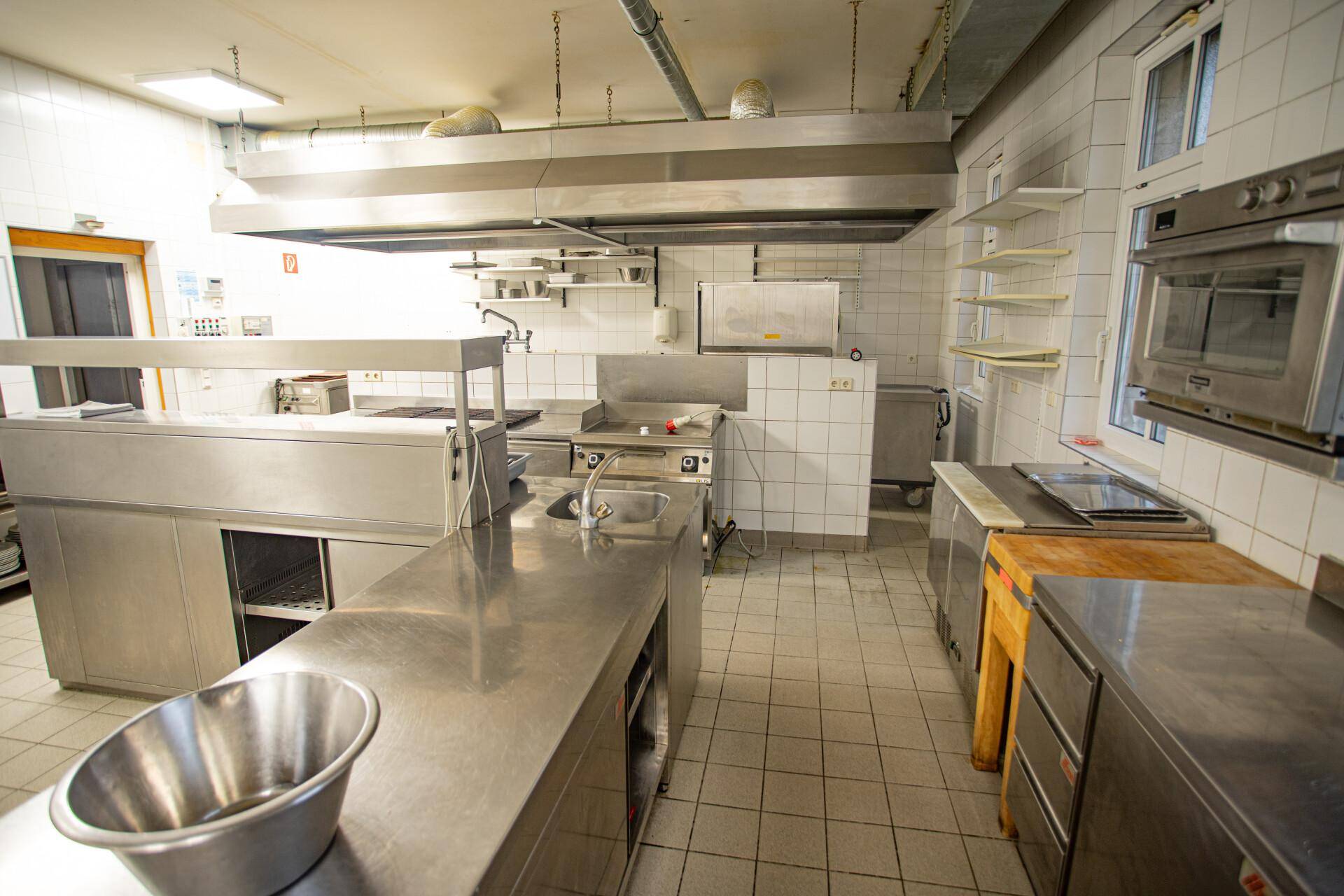 Gut ausgestattete Gastroküche mit mehreren Arbeitsbereichen, Edelstahloberflächen und professionellen Geräten.