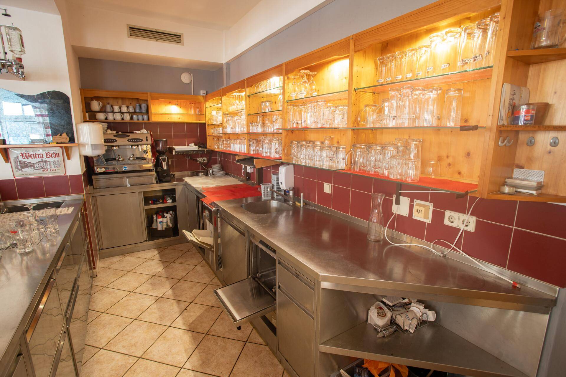 Professionelle Gastroküche mit Edelstahloberflächen, Spülbecken und Regalen voller Gläser, gut ausgestattet.
