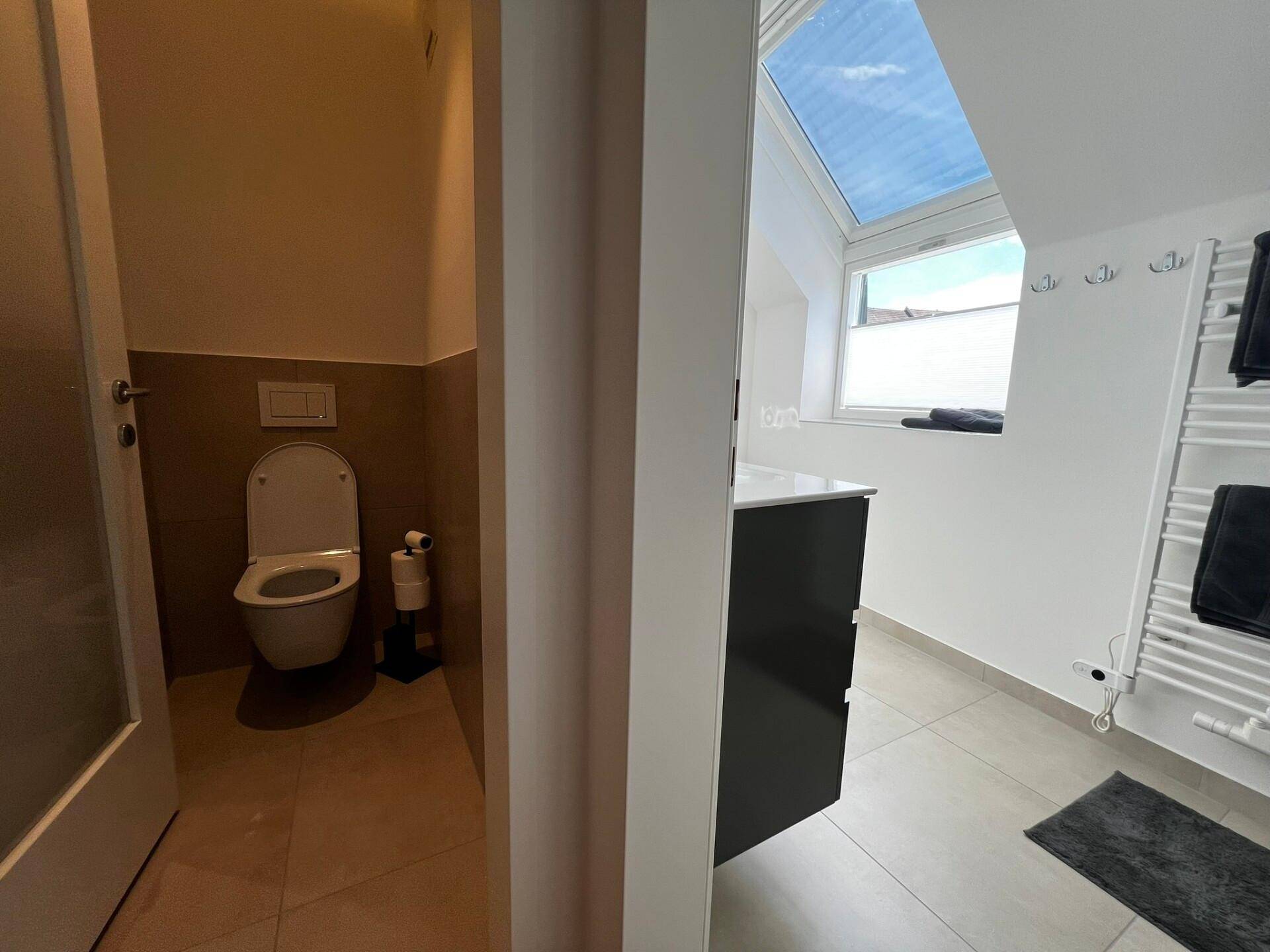 Modernes Badezimmer mit Dachfenster, Waschtisch und separatem WC-Bereich unter einer Dachschräge.