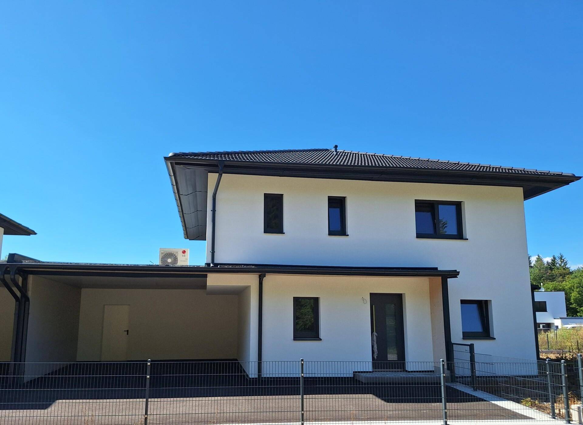 Vorderansicht eines modernen Neubaus mit Carport und dunklem Dach.