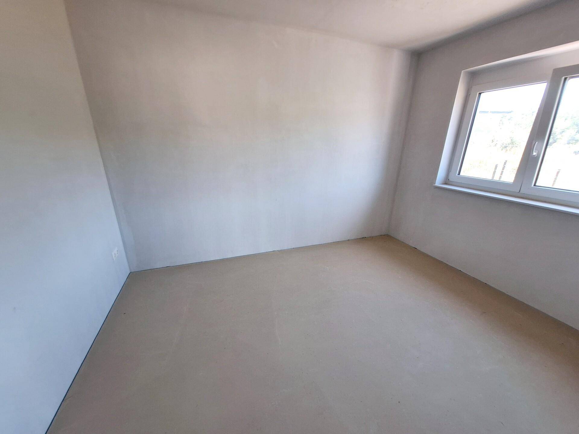 Unmöbliertes Schlafzimmer im Rohbauzustand mit Fenster und hellem Betonboden.