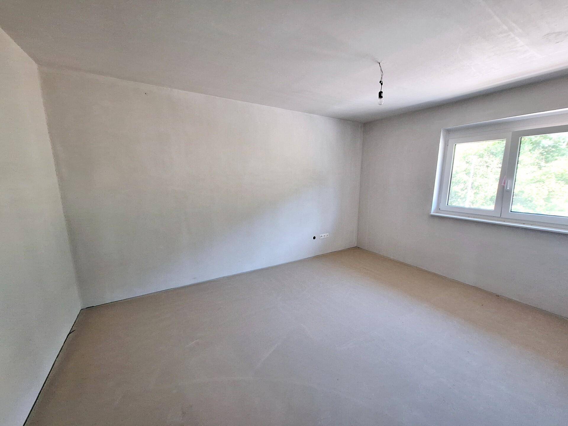 Helles Schlafzimmer im Rohbau mit Fenster und unfertigem Bodenbelag.