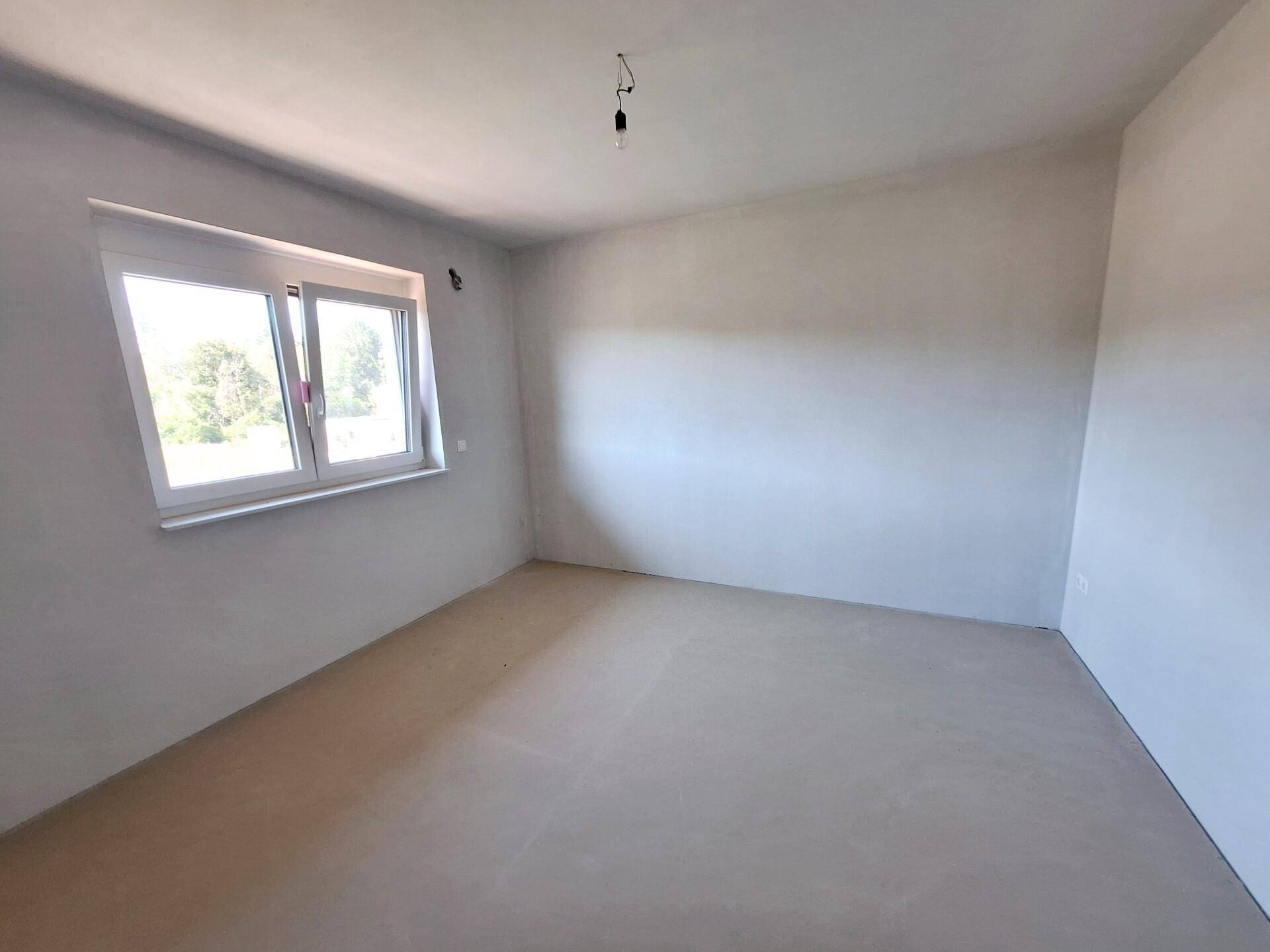 Unmöblierter Raum im Neubau mit Fenster und Betonboden, bereit für den Ausbau.