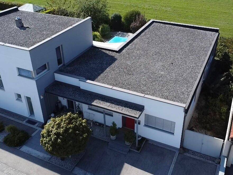 Luftaufnahme eines modernen Gebäudes mit Flachdach, umgeben von Grünflächen und einem angrenzenden Poolbereich.