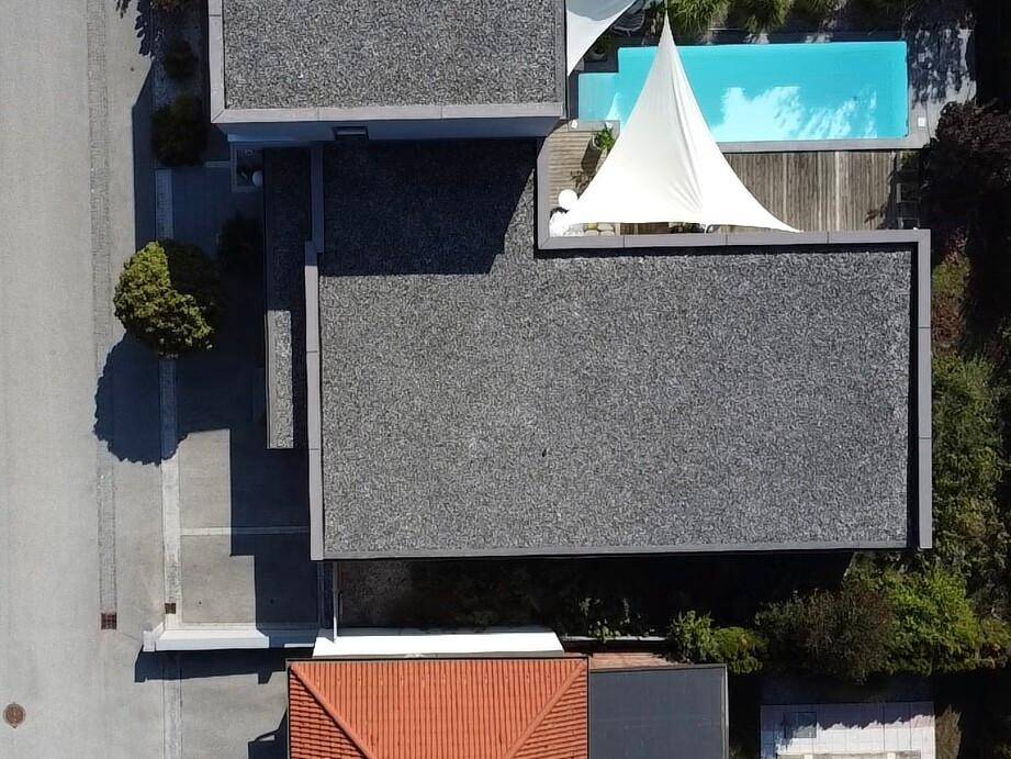 Vogelperspektive des Anwesens mit modernem Flachdach, einem Poolbereich und Holzdeck.