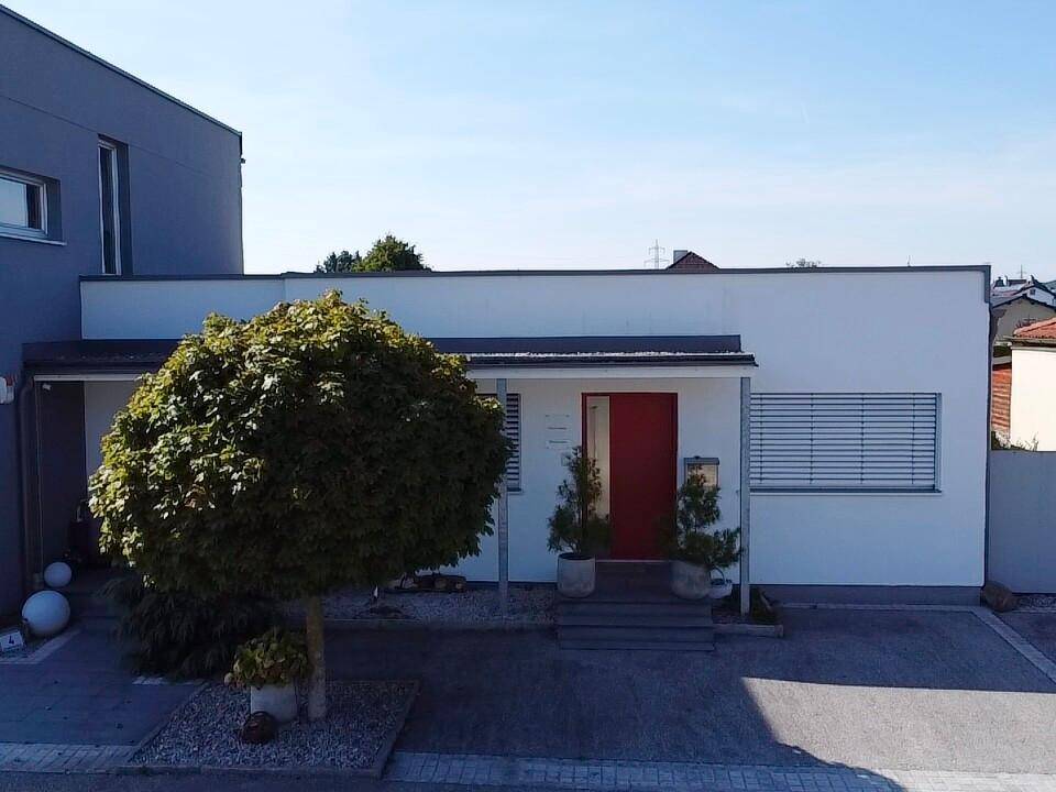 Frontansicht eines modernen Gebäudes mit roter Eingangstür und gepflegter Außenanlage unter blauem Himmel.