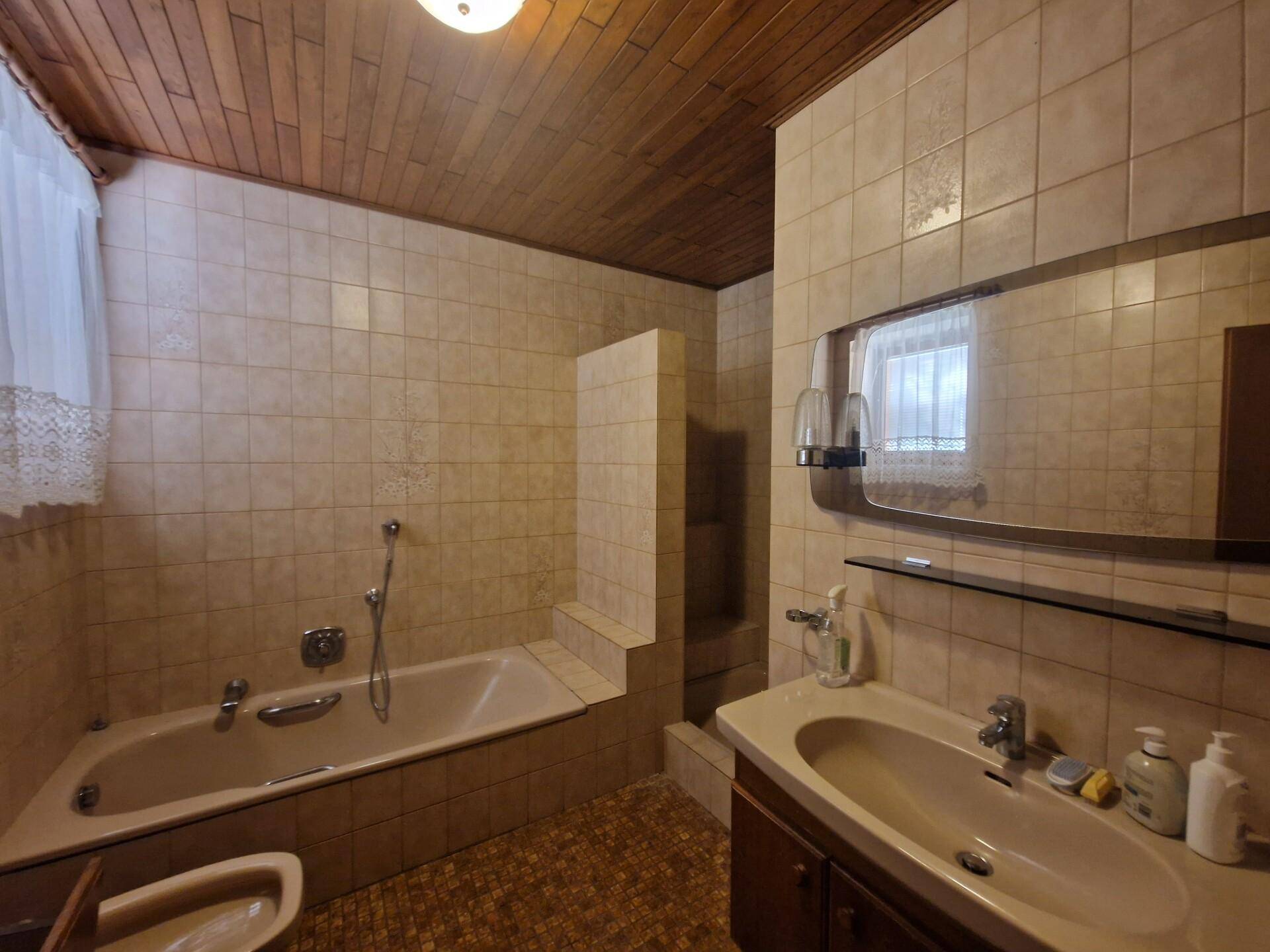 Badezimmer mit Badewanne, Waschbecken, beigen Fliesen und Holzdecke.
