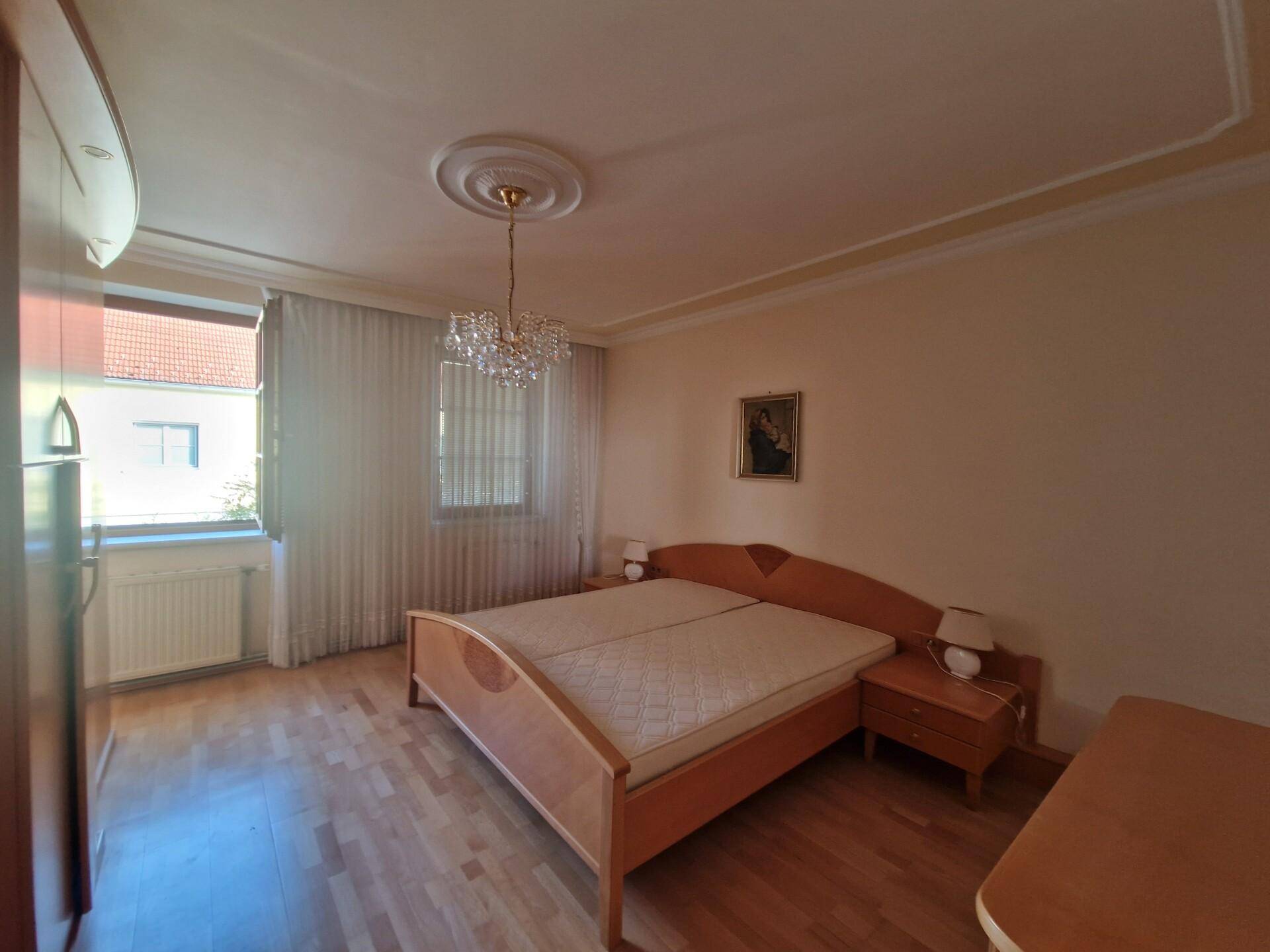 Schlafzimmer mit Doppelbett, Parkettboden und einer dekorativen Deckenrosette.
