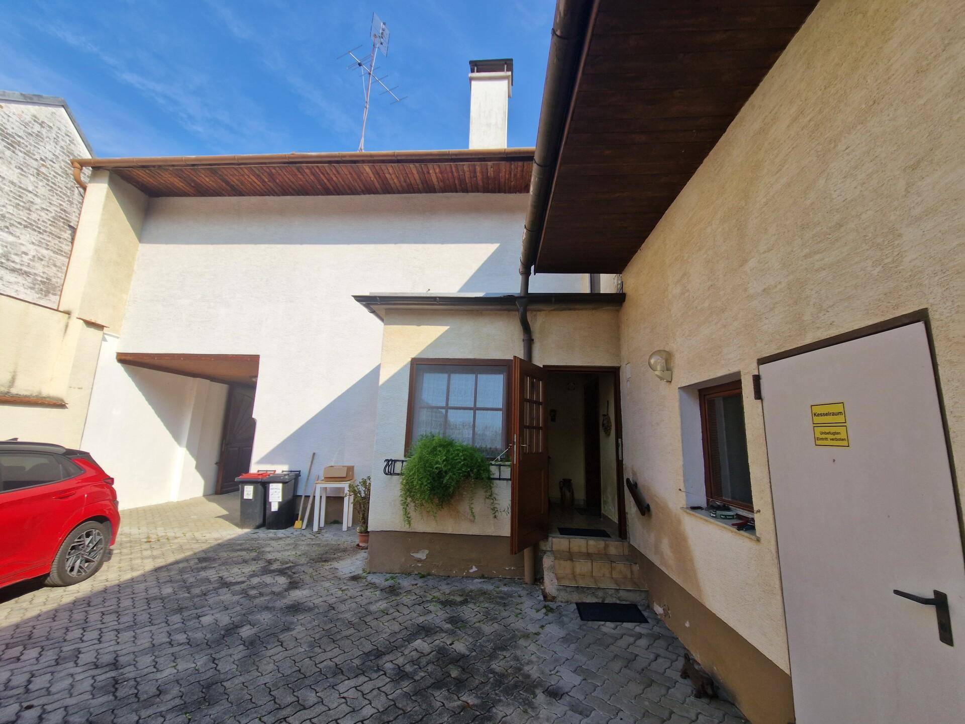 Gepflasterter Innenhof mit Nebengebäuden und Eingangsbereich unter blauem Himmel.