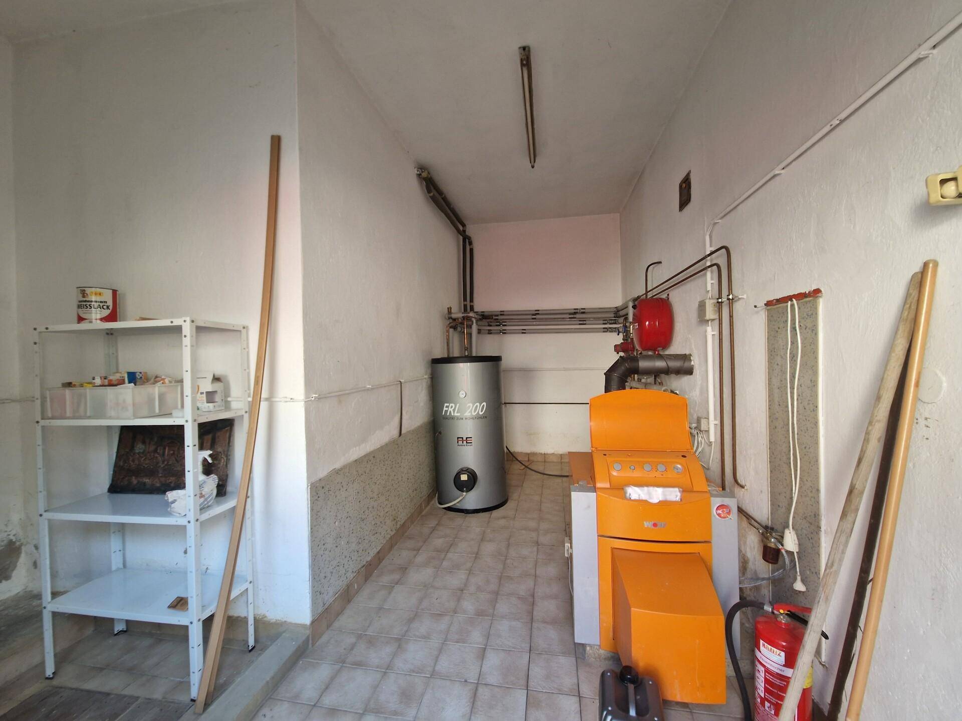 Heizraum mit Heizungsanlage, Boiler und Lagerregalen auf Fliesenboden.
