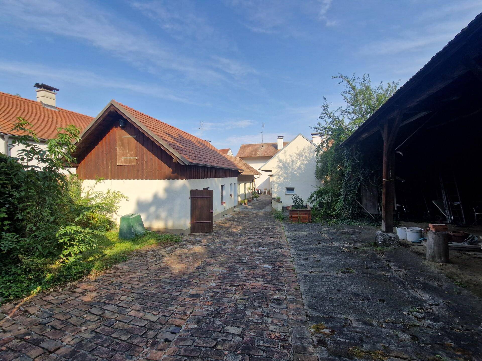 Gepflasterter Hof zwischen den Gebäuden mit einer Scheune und üppigem Grün.