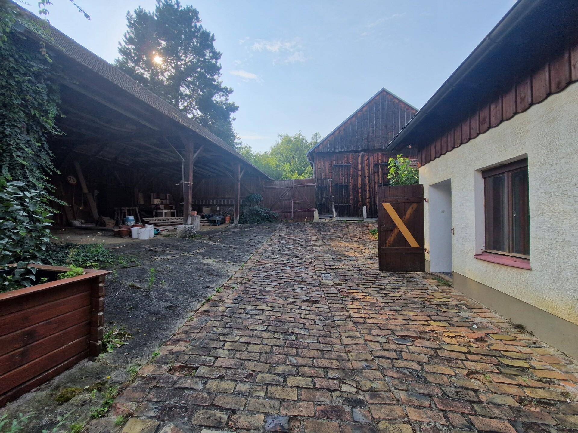 Gepflasterter Hof mit einer Scheune im Hintergrund und einem Holztor.