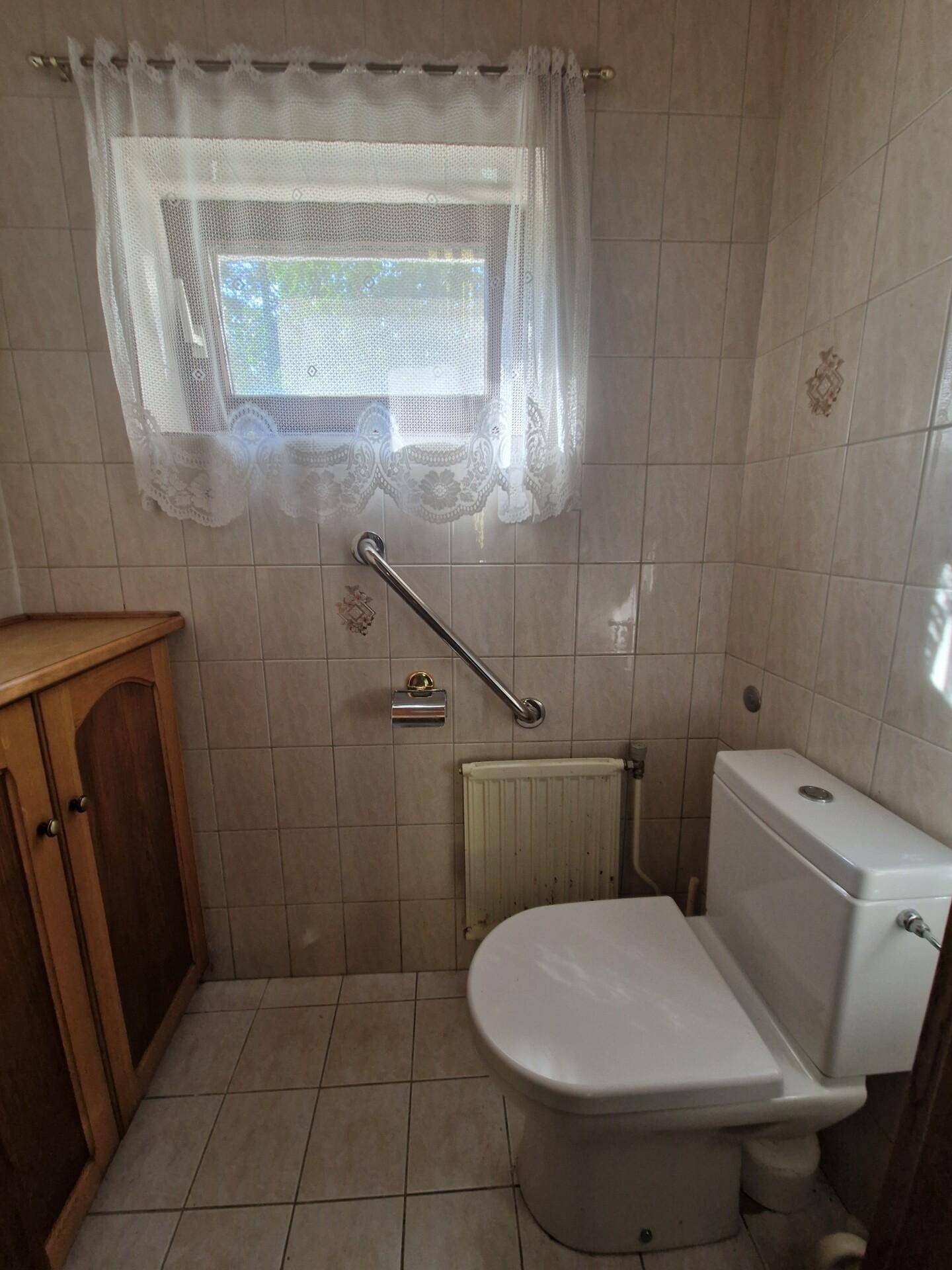 Separates WC mit Haltegriffen, Fenster und hellen Fliesen an den Wänden.