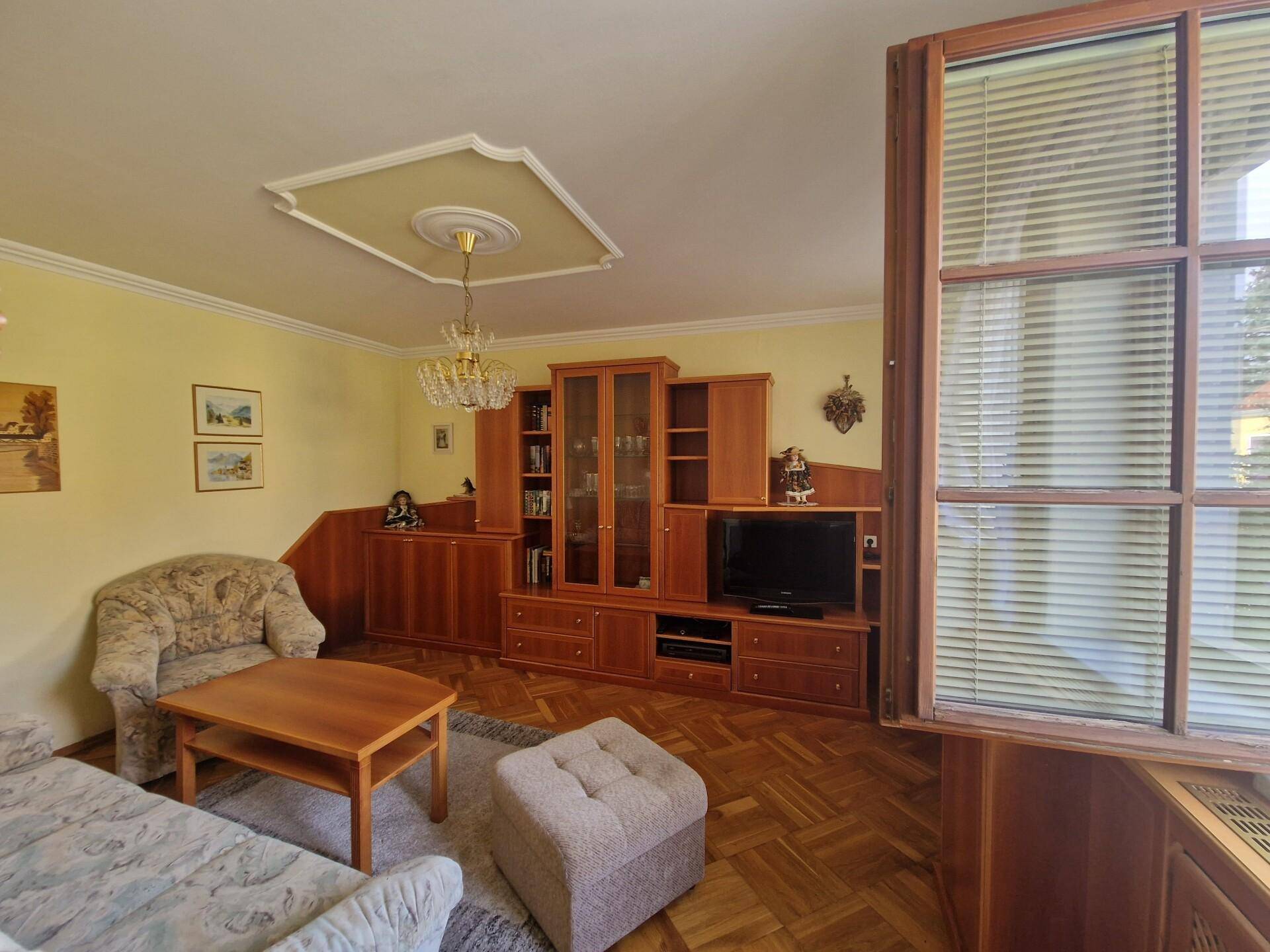 Wohnzimmer mit Parkettboden, traditionellen Holzmöbeln und einer Stuckdecke.