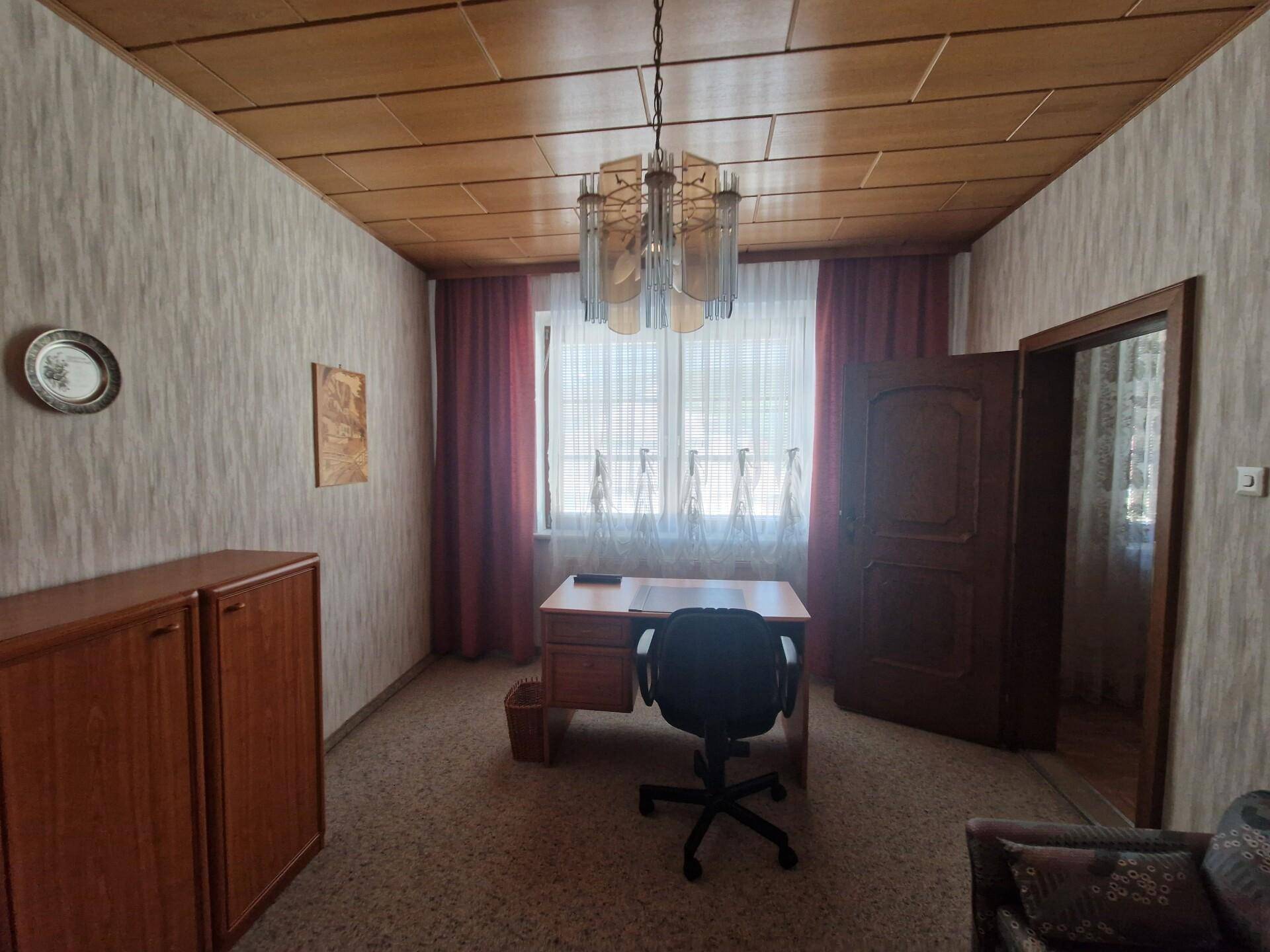 Büro mit Holzdecke, Schreibtisch und gemusterten Tapeten an den Wänden.