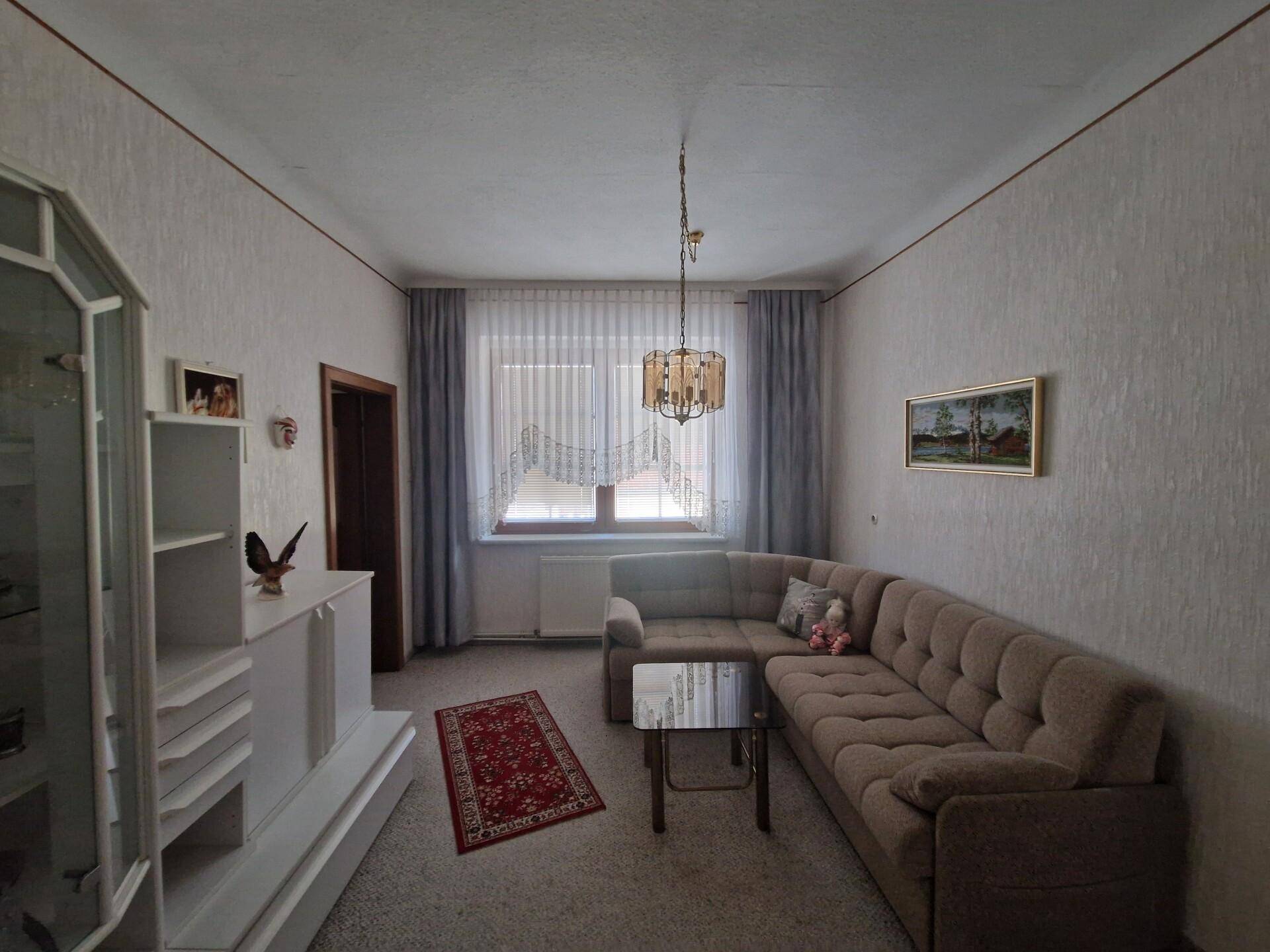 Wohnzimmer mit Ecksofa, Teppichboden und einem modernen Deckenleuchter.