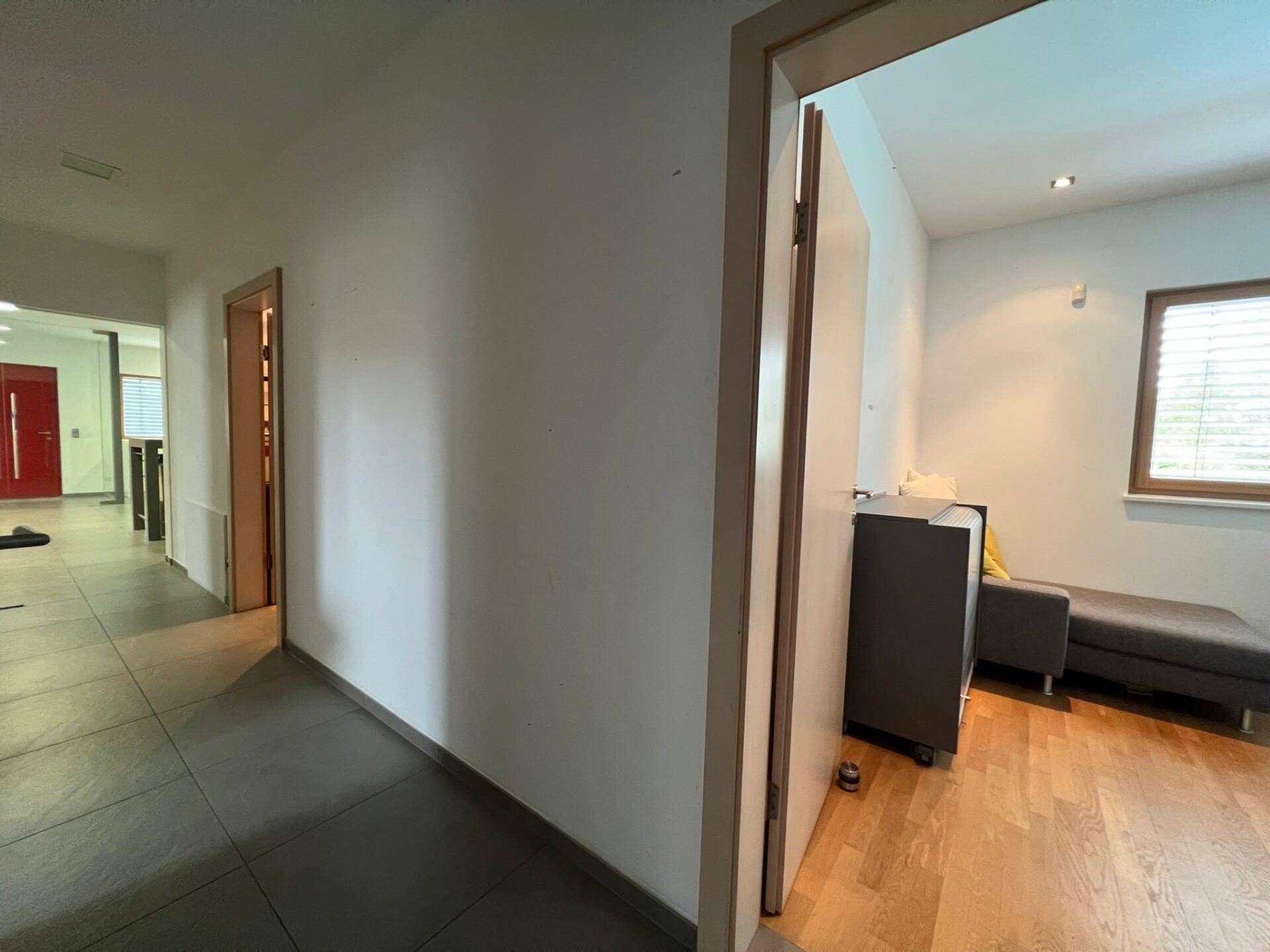 Heller Flur mit Fliesenboden, der zu weiteren Räumen führt, darunter ein Büro mit Holzparkett.